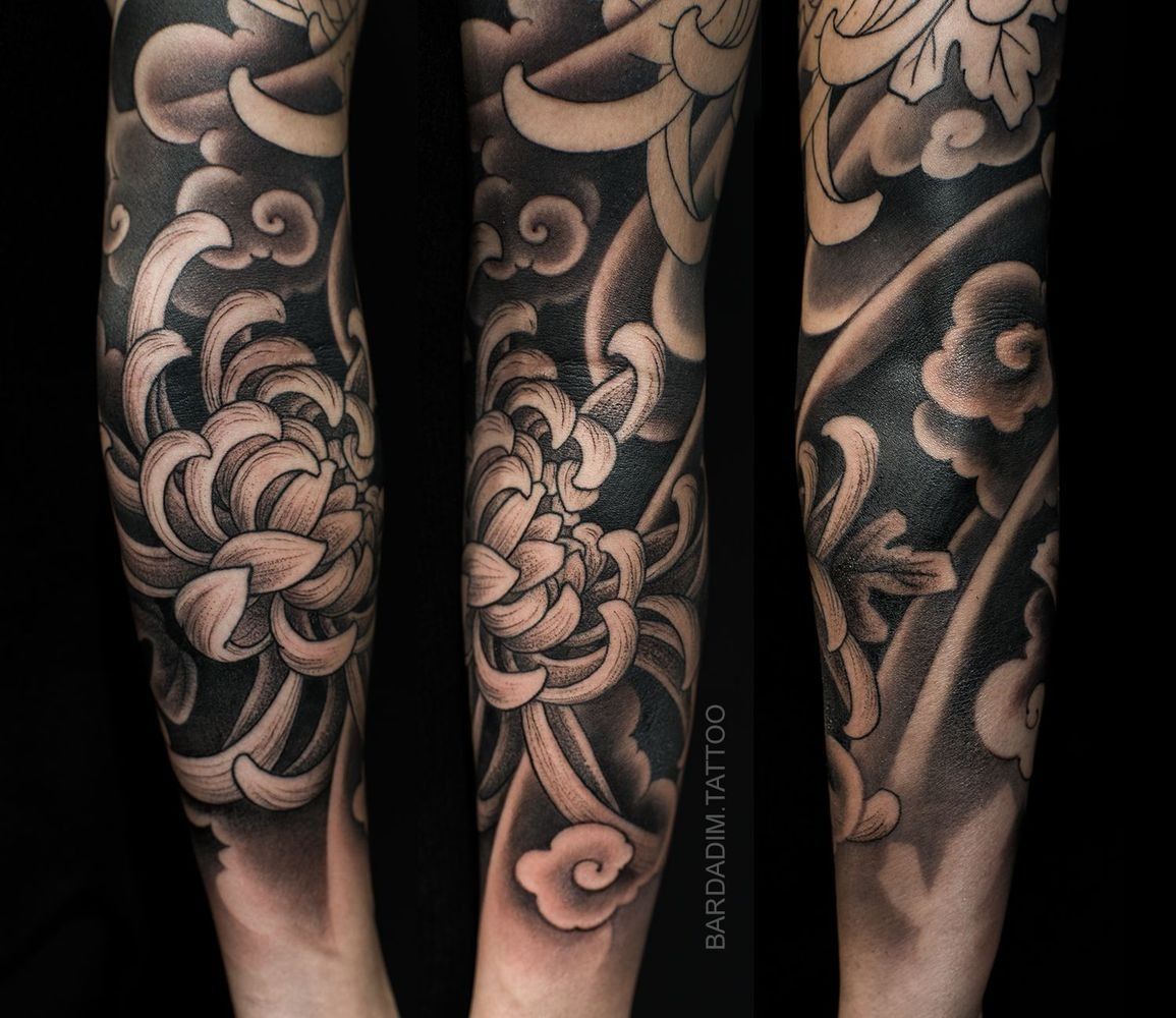 Black and white Japanese-style floral tattoo on arm, featuring chrysanthemums, clouds, and swirling patterns.