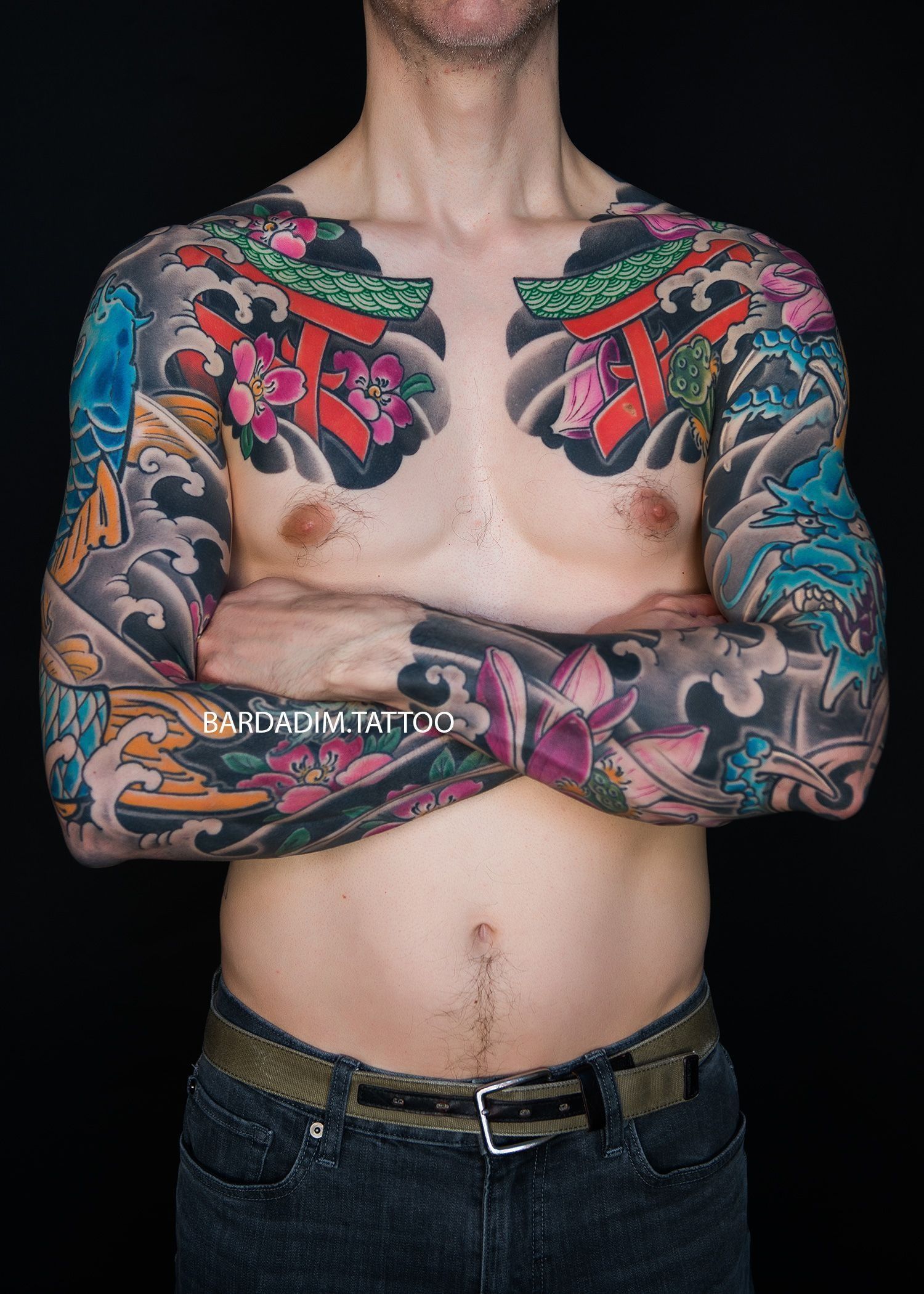Man with arms crossed, torso and sleeves covered in colorful Japanese tattoos.