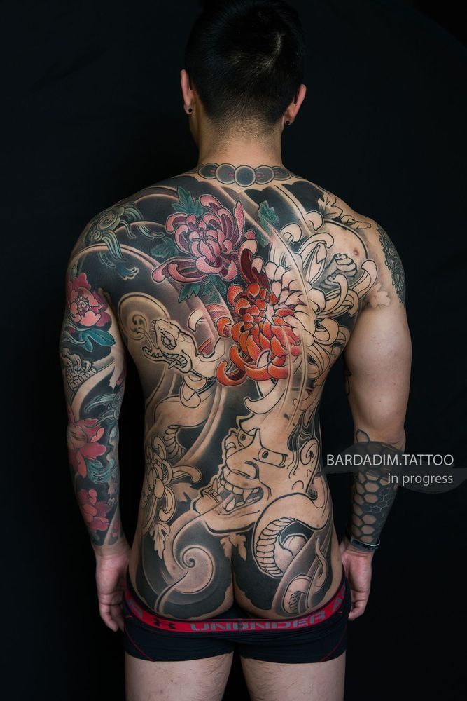 Man's back covered in Japanese-style tattoo art of Hannya mask and snake surrounded with chrysanthemum flowers and dark shading in Bardadim Tattoo Studio