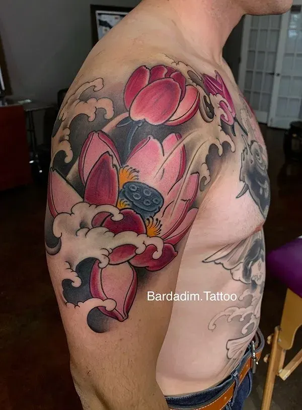 Tattoo of a pink lotus flower with a dark seed pod, waves, and dark accents on a person's shoulder and arm.