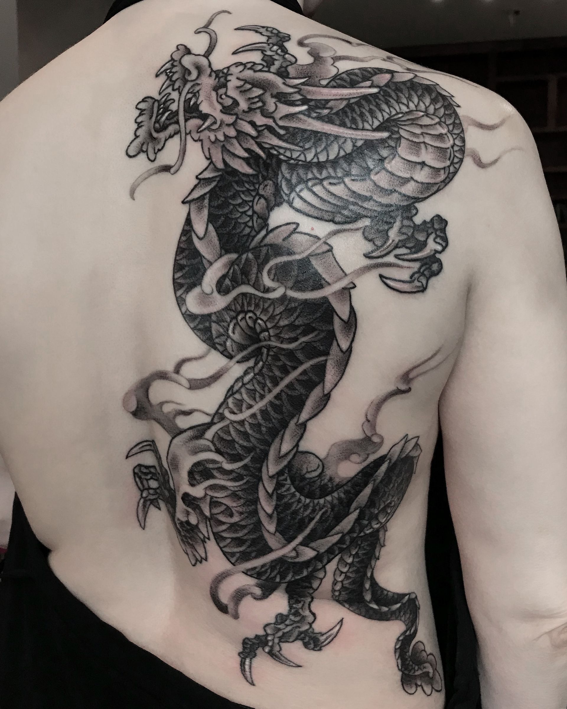 Black and gray dragon tattoo on a person's back.