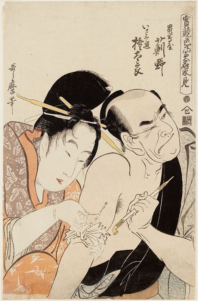 Man tattooing a woman's arm; both in traditional clothing. Tattoo artist close to her, holding tools.