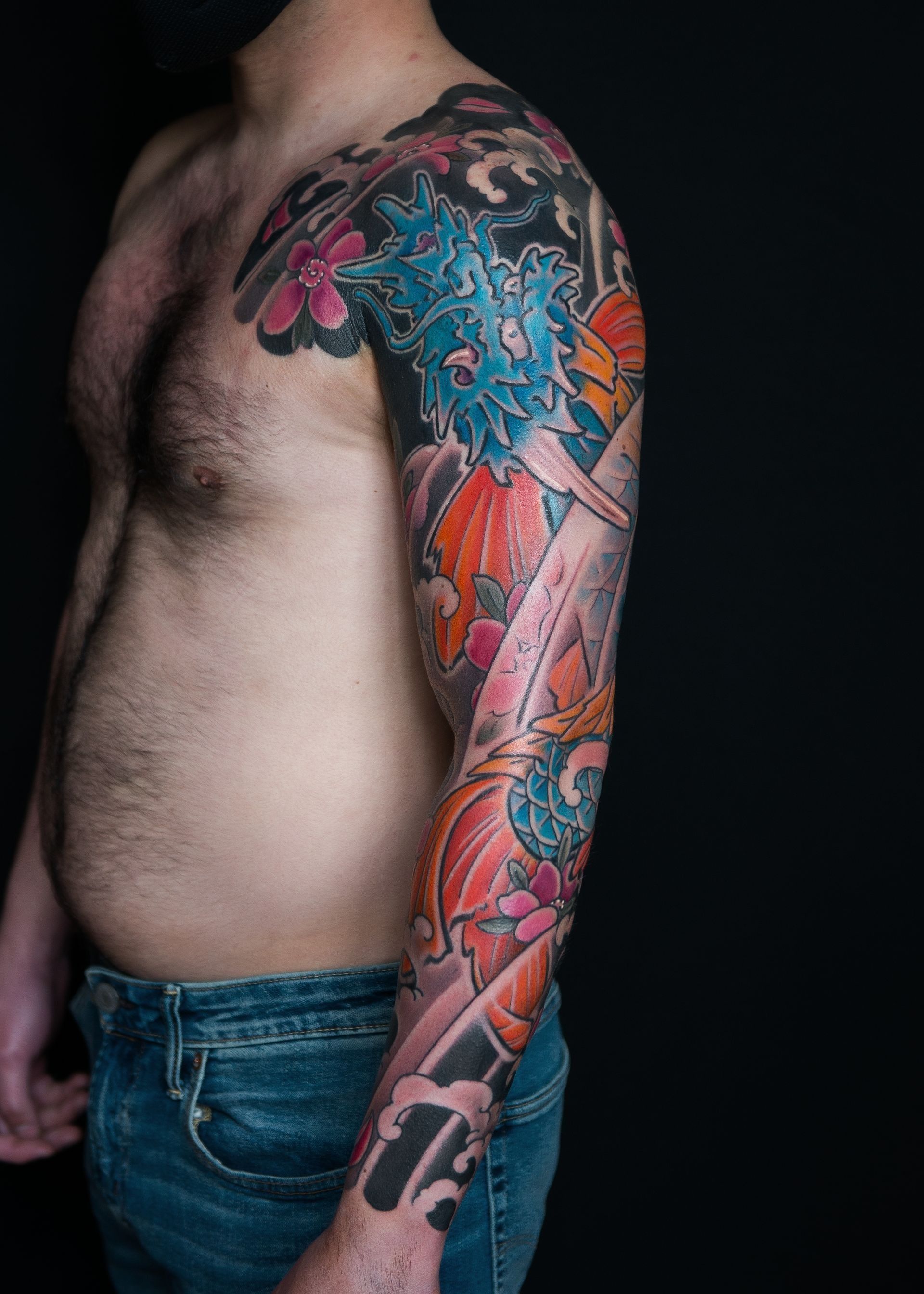 A shirtless man with a colorful tattoo on his arm and shoulder.