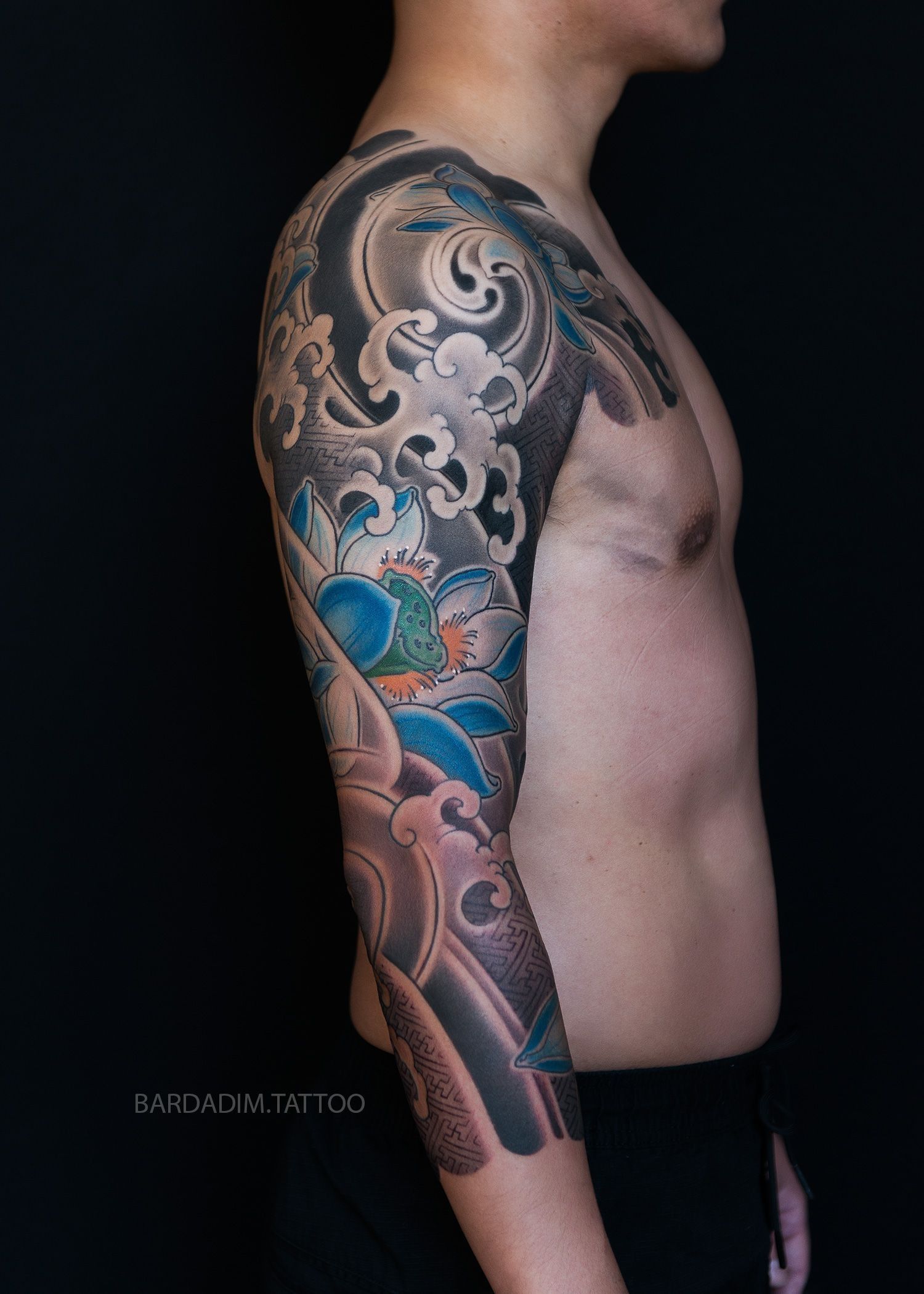 Person with full sleeve tattoo, mostly black, gray, and blue, against a black background.
