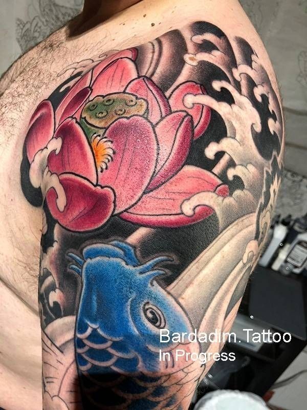 A man has a tattoo of a lotus flower and a fish on his shoulder.