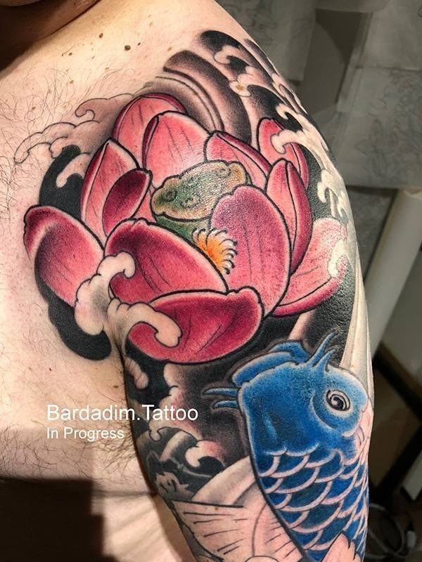 A man has a tattoo of a lotus flower and a fish on his shoulder.