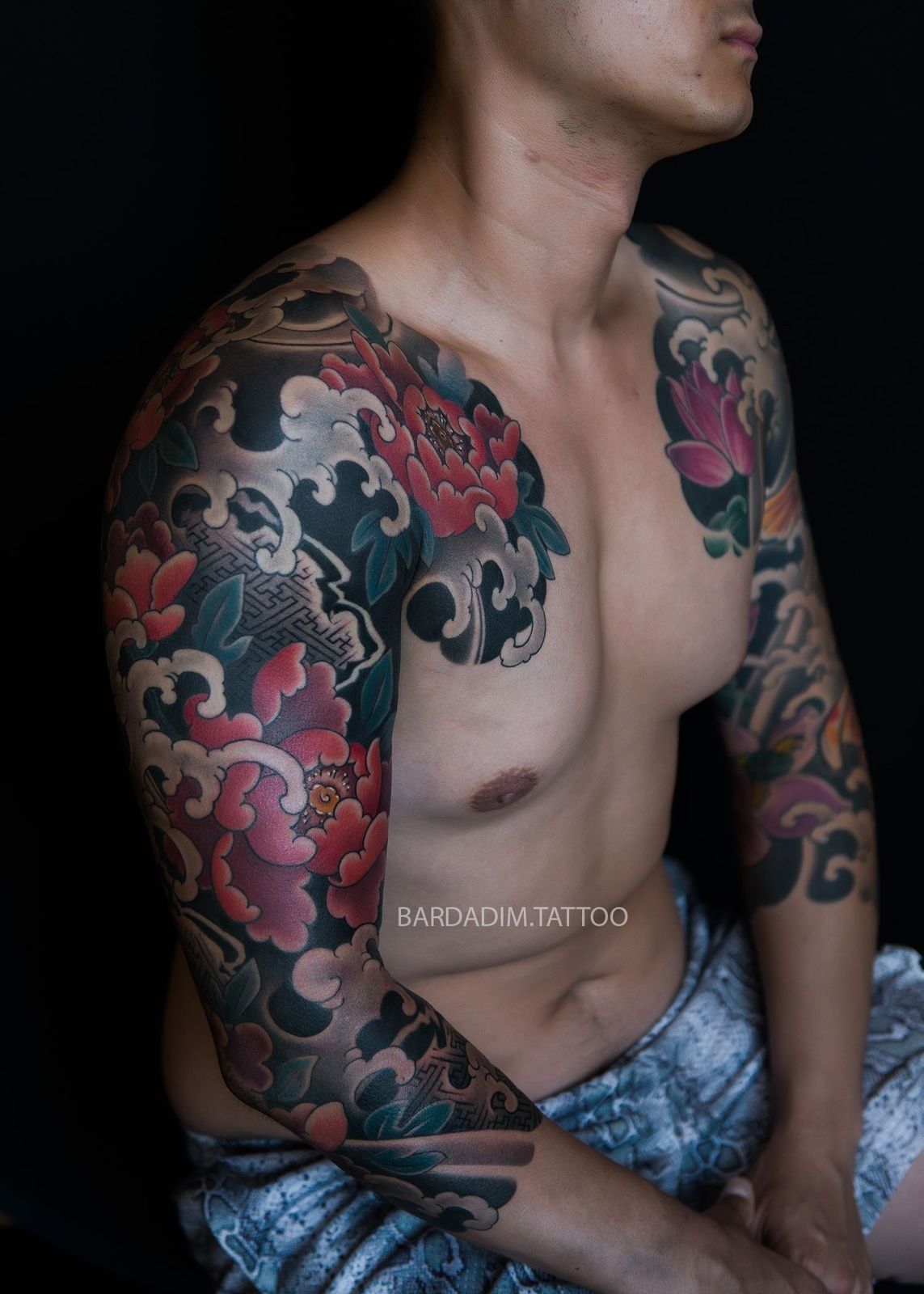 A shirtless man with a tattoo on his arm and chest.