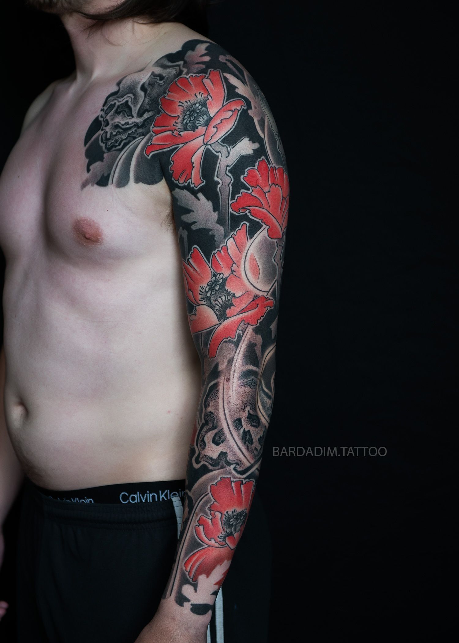 A shirtless man with a full sleeve tattoo on his arm.