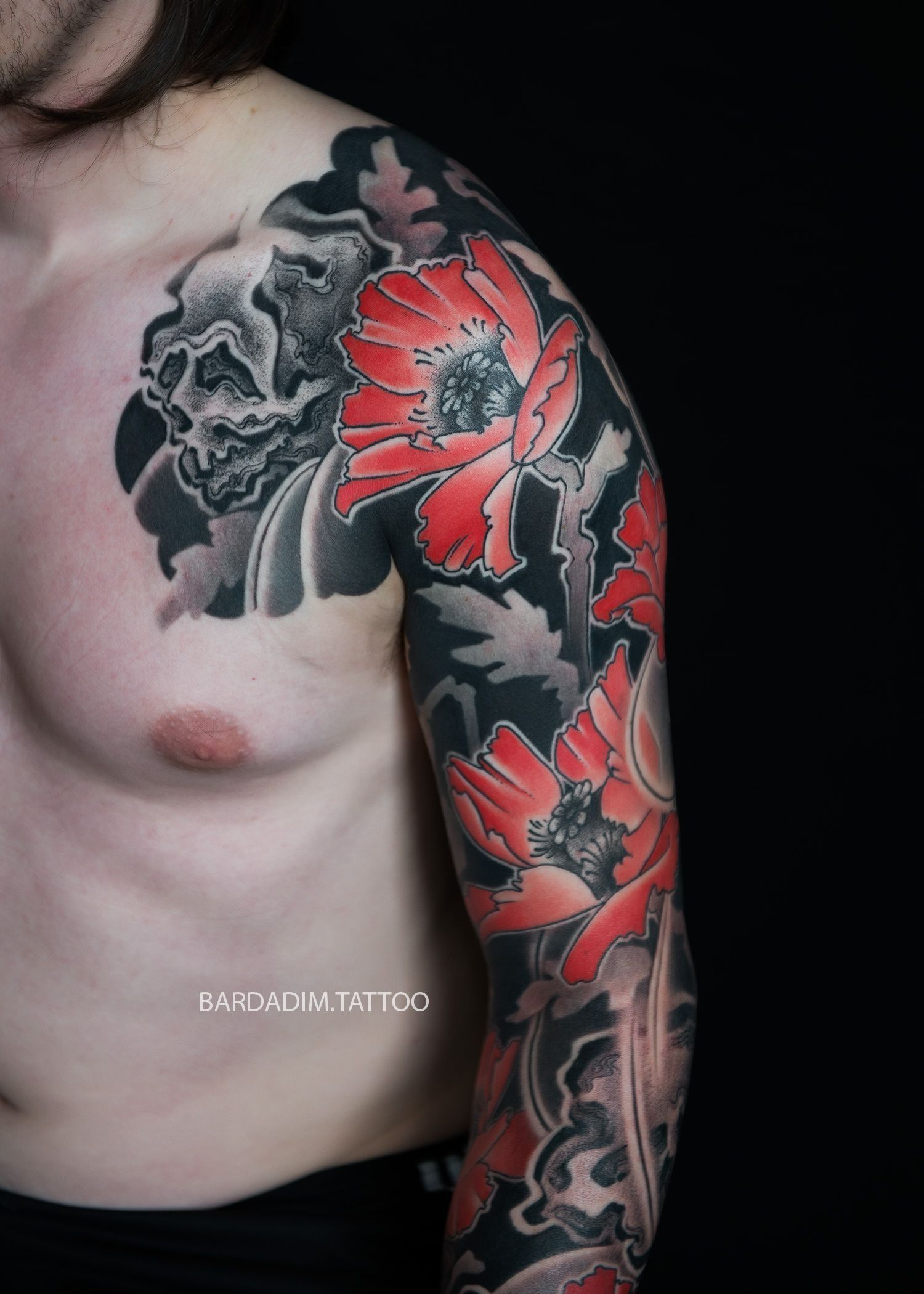 A man has a tattoo of red and black flowers on his arm.