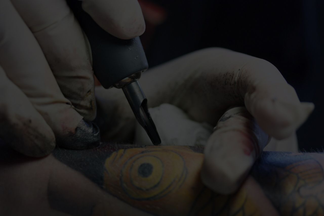Close-up of George Bardadim's gloved hands using a tattoo machine to create an Irezumi design on skin.