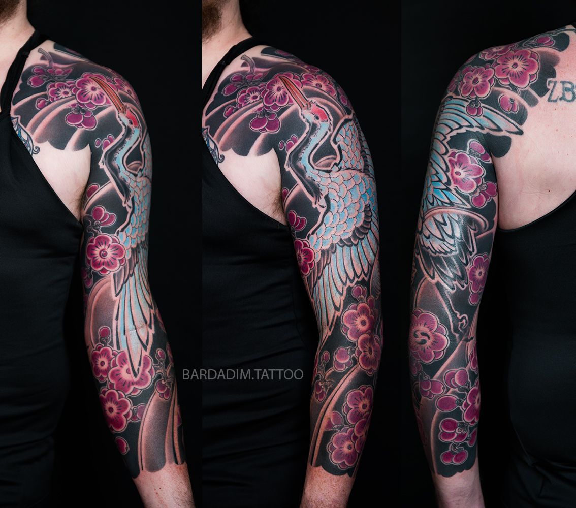 Tattoo sleeve with crane, blossoms. Gray, pink, black. Man in black tank top.