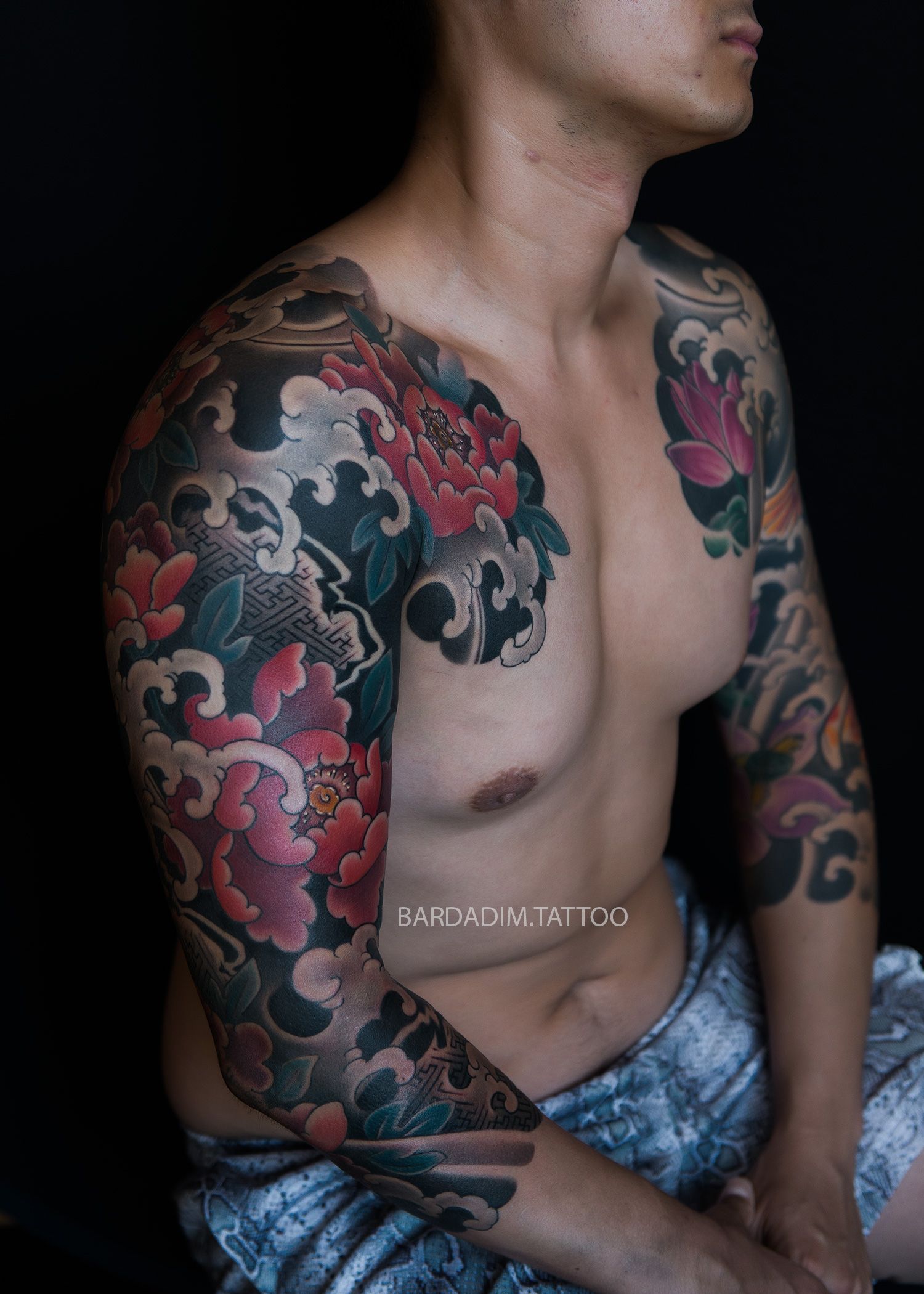 Man with a large, colorful floral and cloud Japanese style tattoo on his arm, chest, and shoulder.