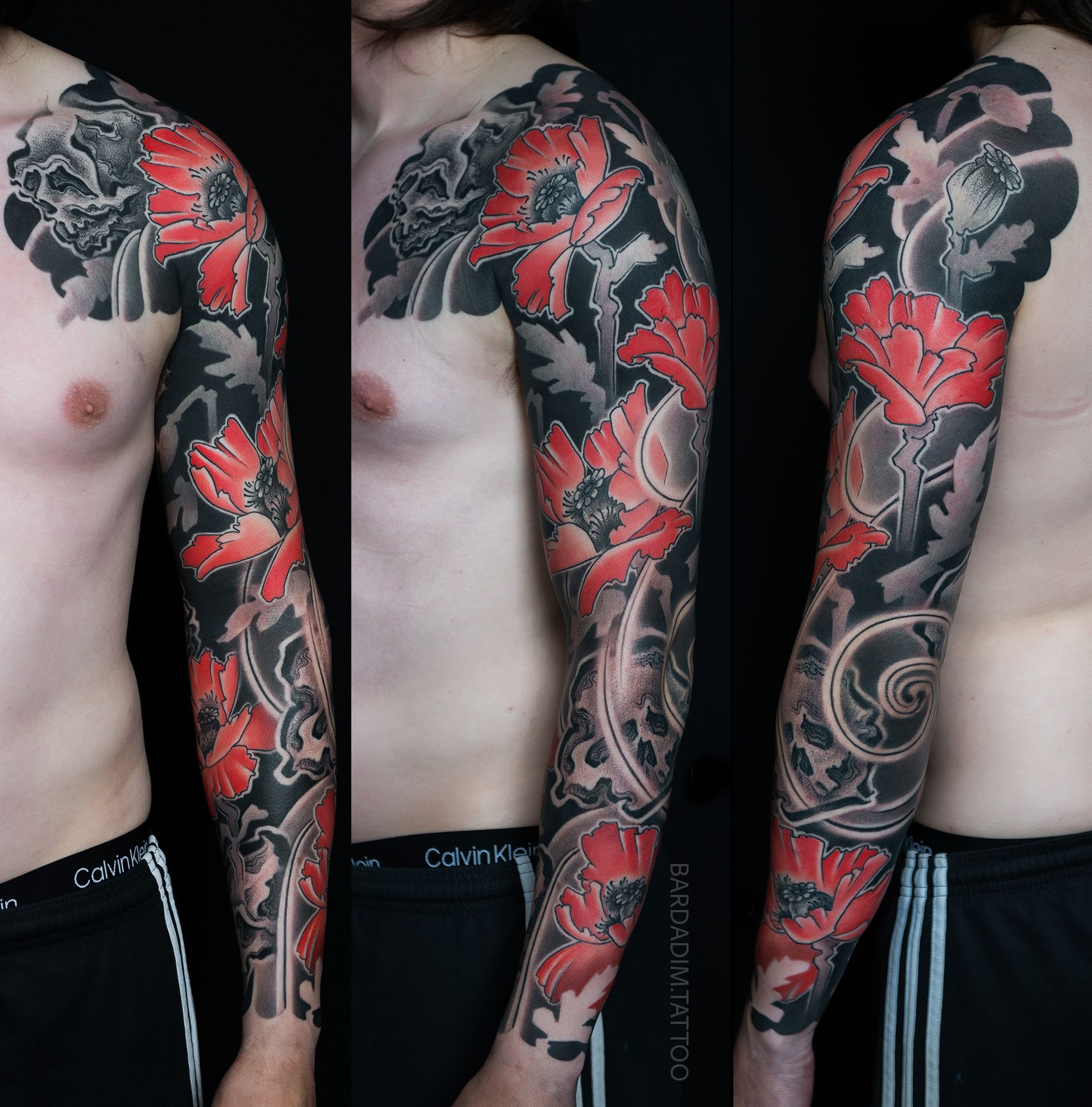 Tattoo of red flowers and gray leaves on a person's full arm, against a black background.