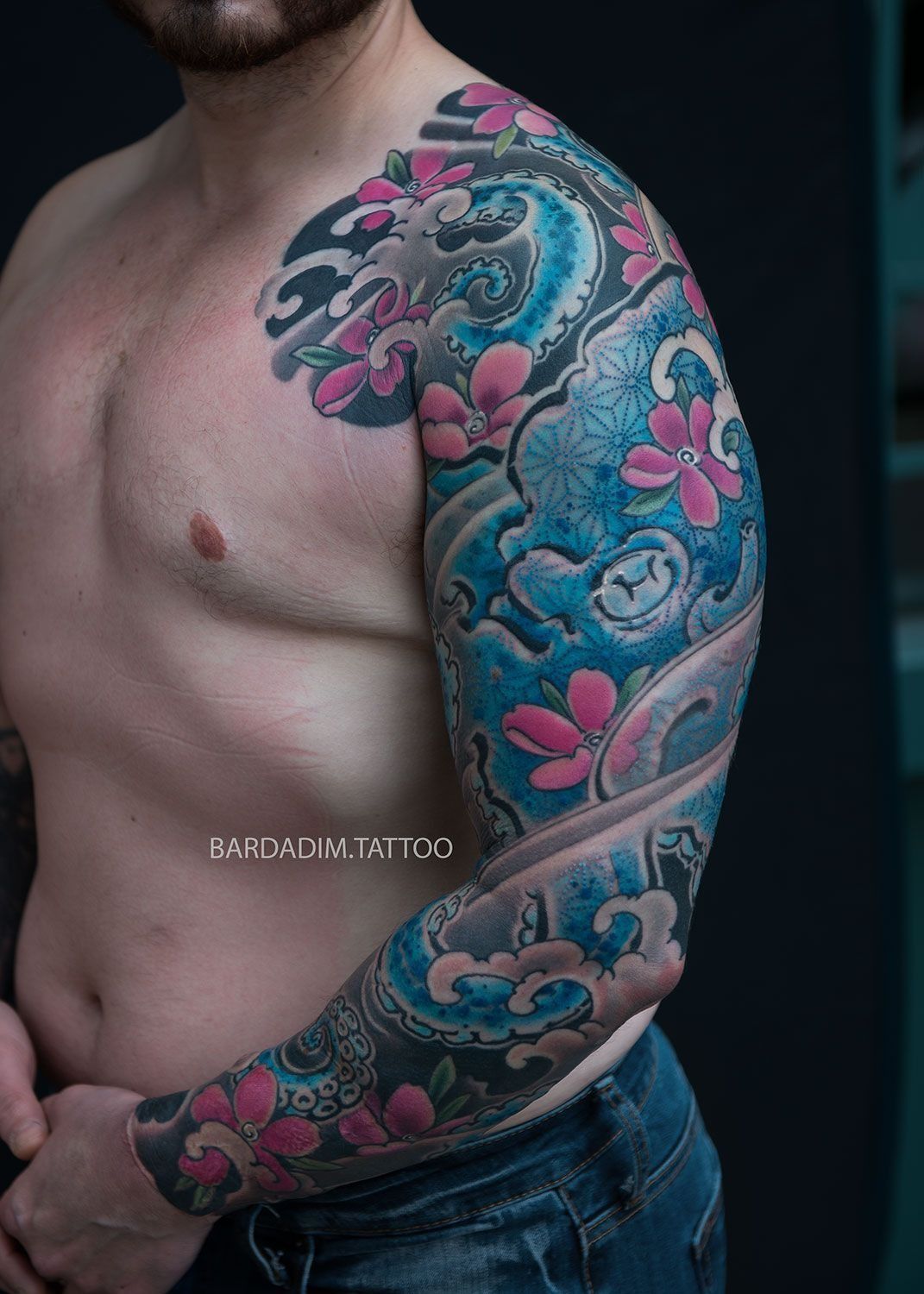 A shirtless man with a full sleeve tattoo on his arm.