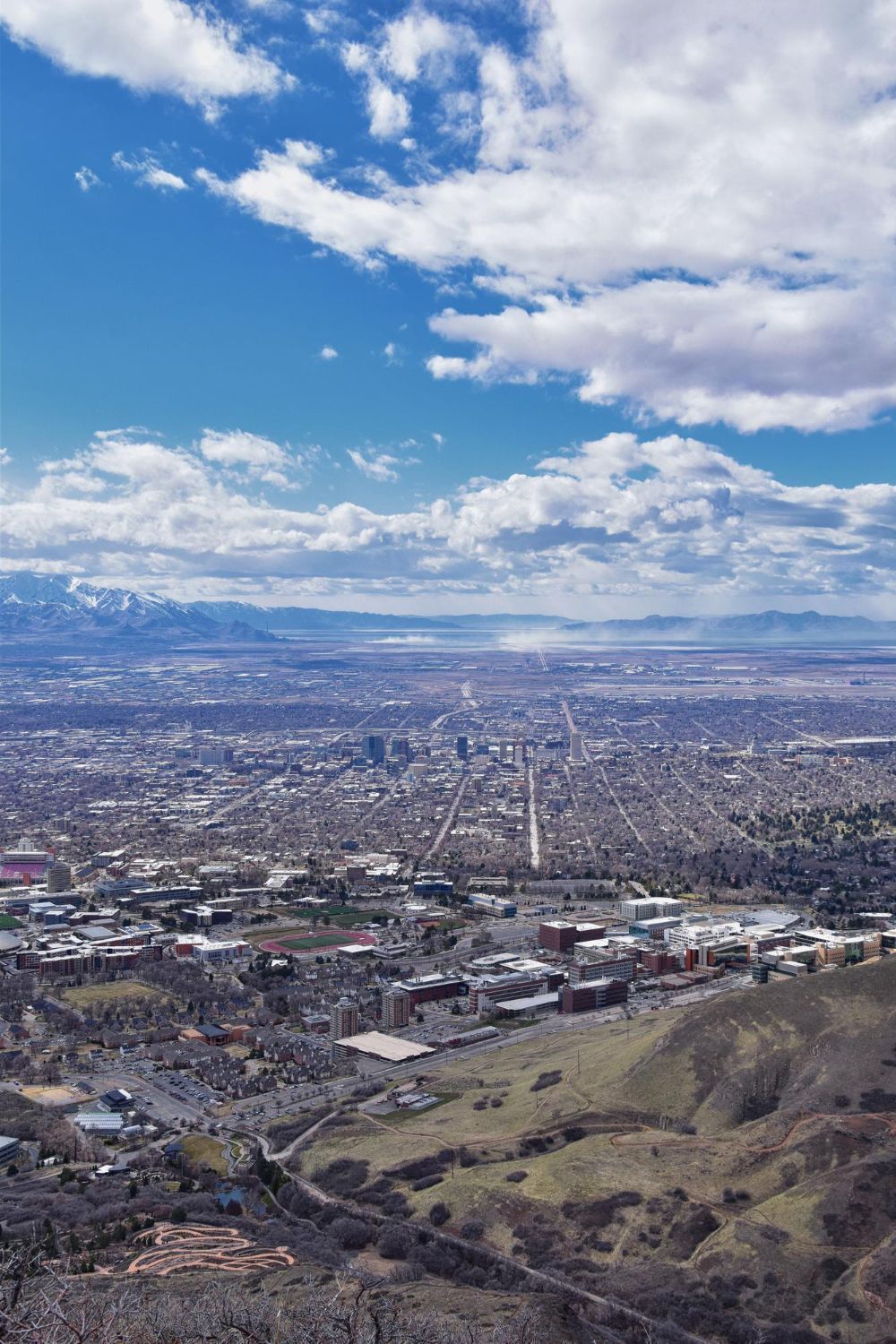 View of Salt Lake City from a hillside on a sunny day, with a bright blue sky and scattered clouds.