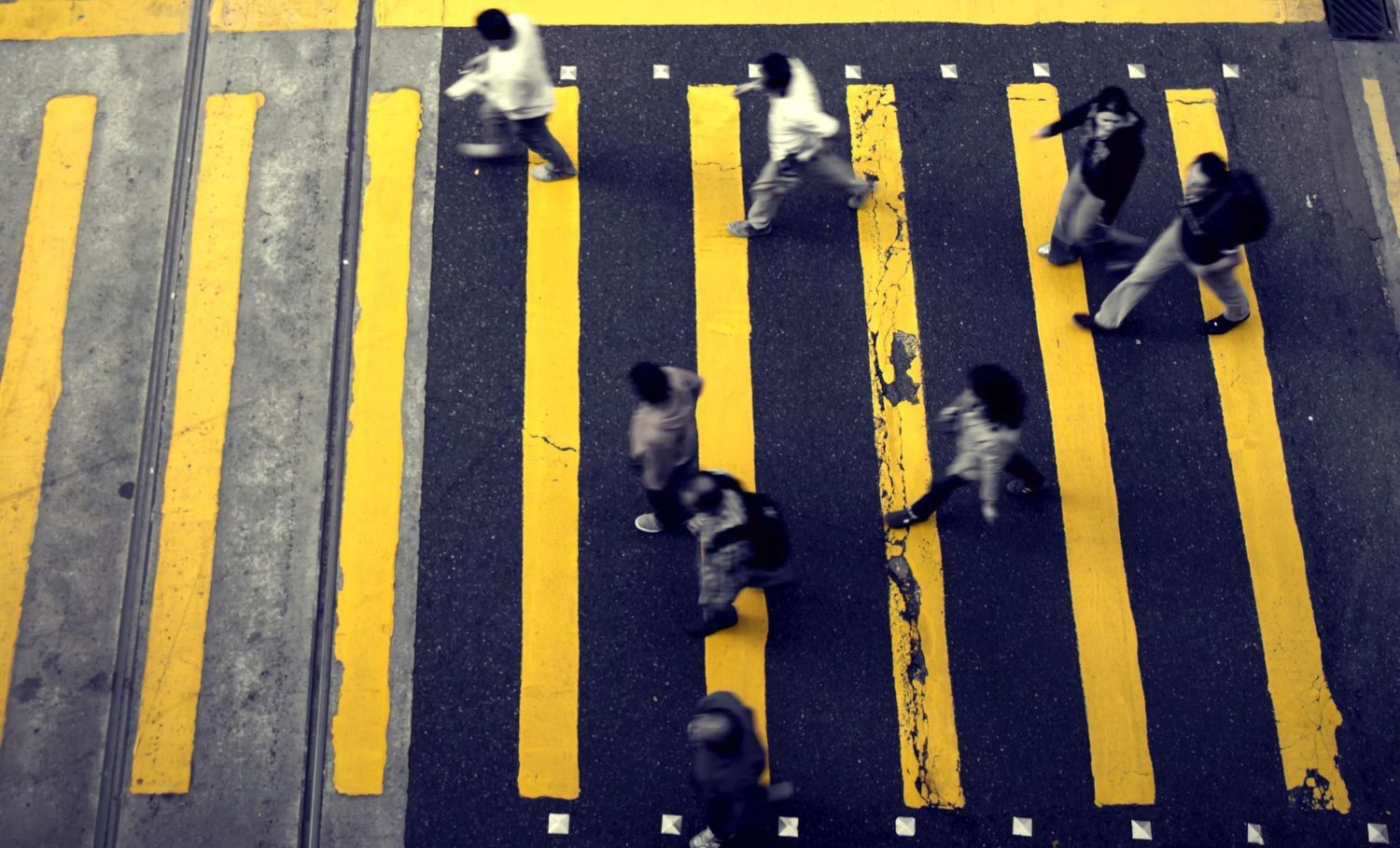 Pedestrians crossing a street at a zebra crossing with yellow lines.