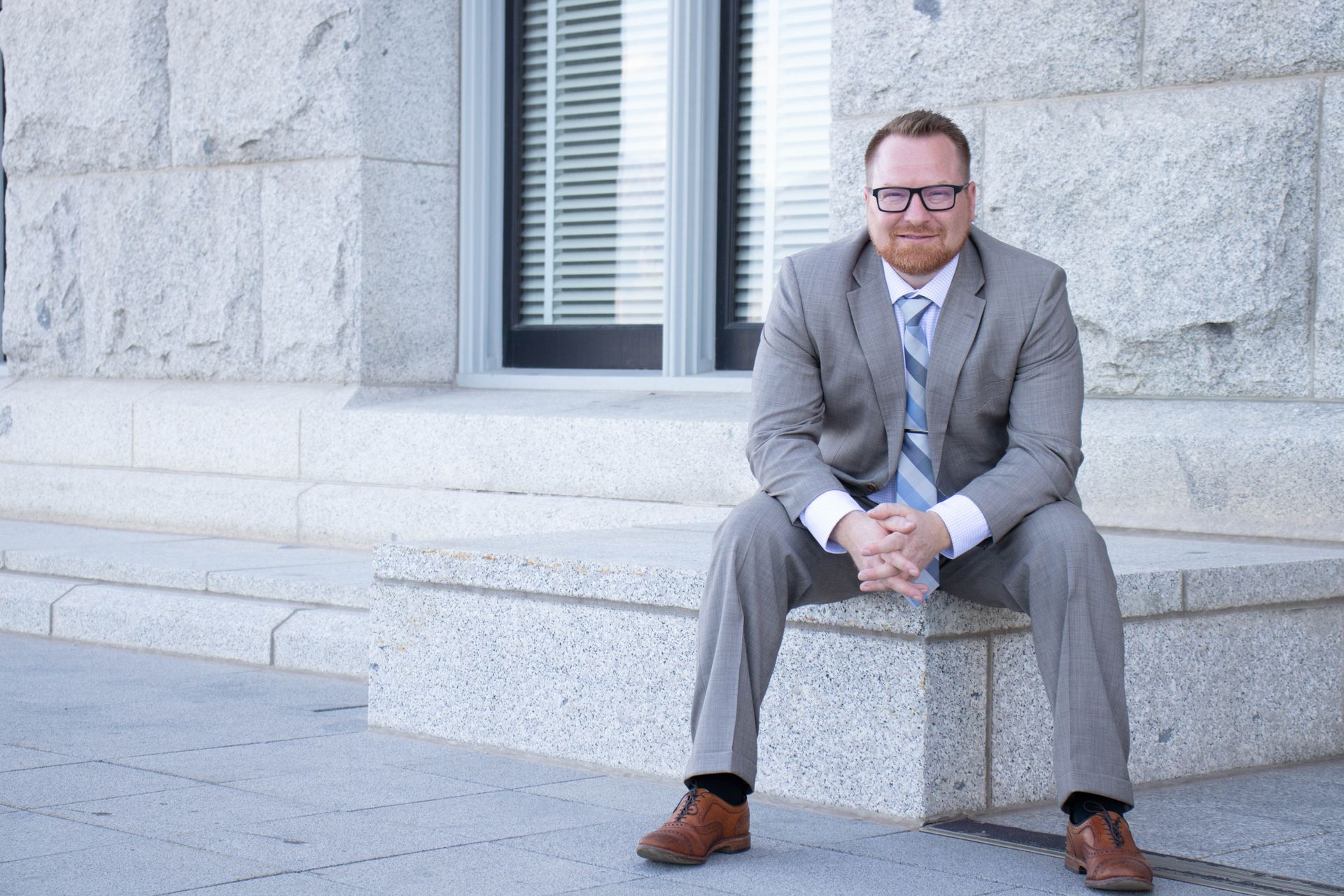 A man in a suit and tie is standing in front of a window.