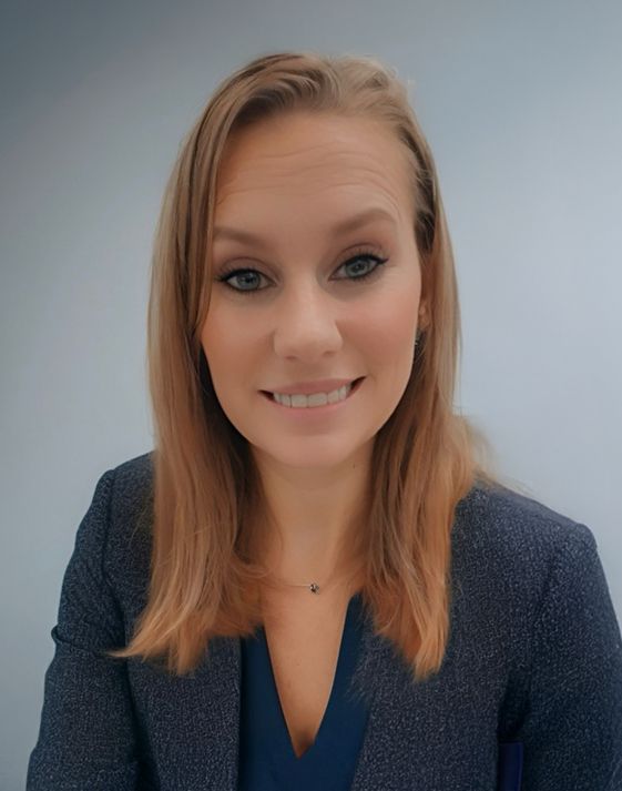 Woman with blonde hair smiling, wearing a blue blazer, against a light blue background.