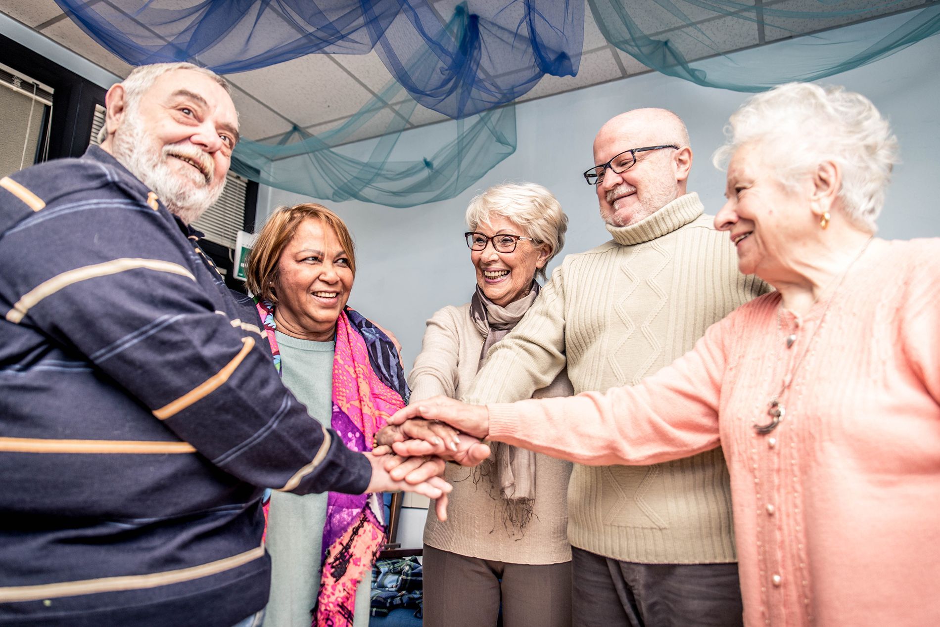Group of senior adults with hands stacked together, smiling in a room.