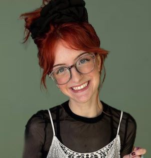 Woman with red hair in a bun, wearing glasses and smiling, in front of a green background.