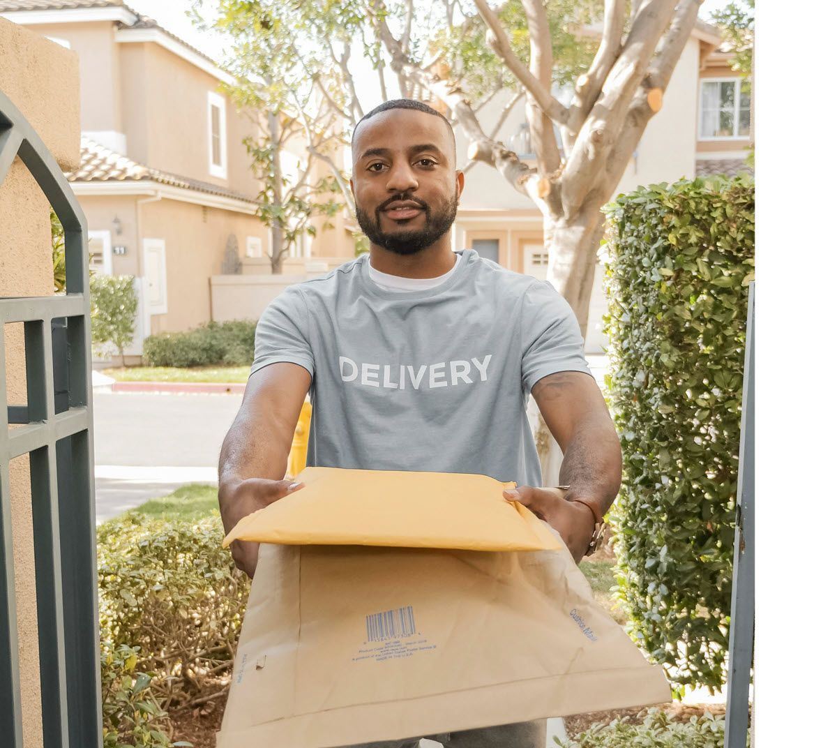 Delivery person holding package, standing in front of a gate. He is wearing a gray shirt.