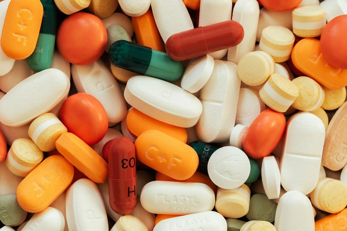 Pills and capsules in various colors: orange, white, green, yellow, red, and brown, scattered together.
