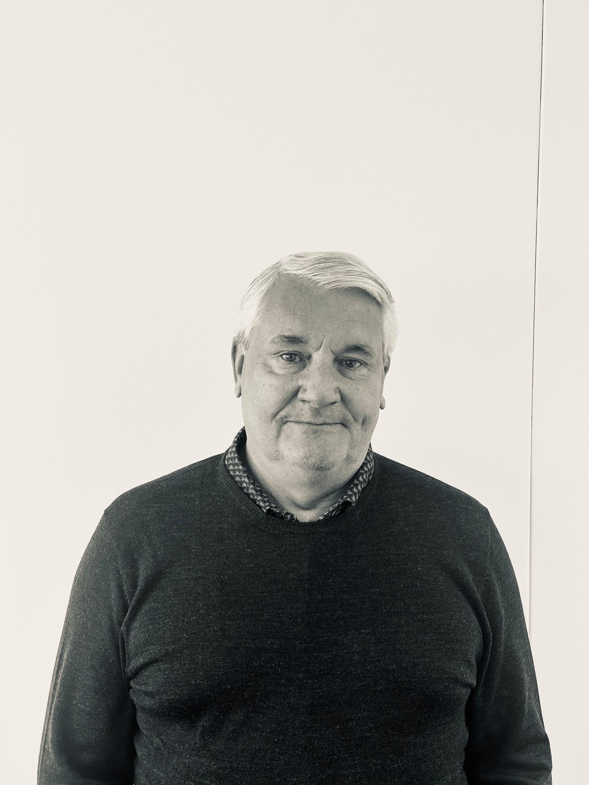Portrait of a man in a dark sweater standing against a light wall.