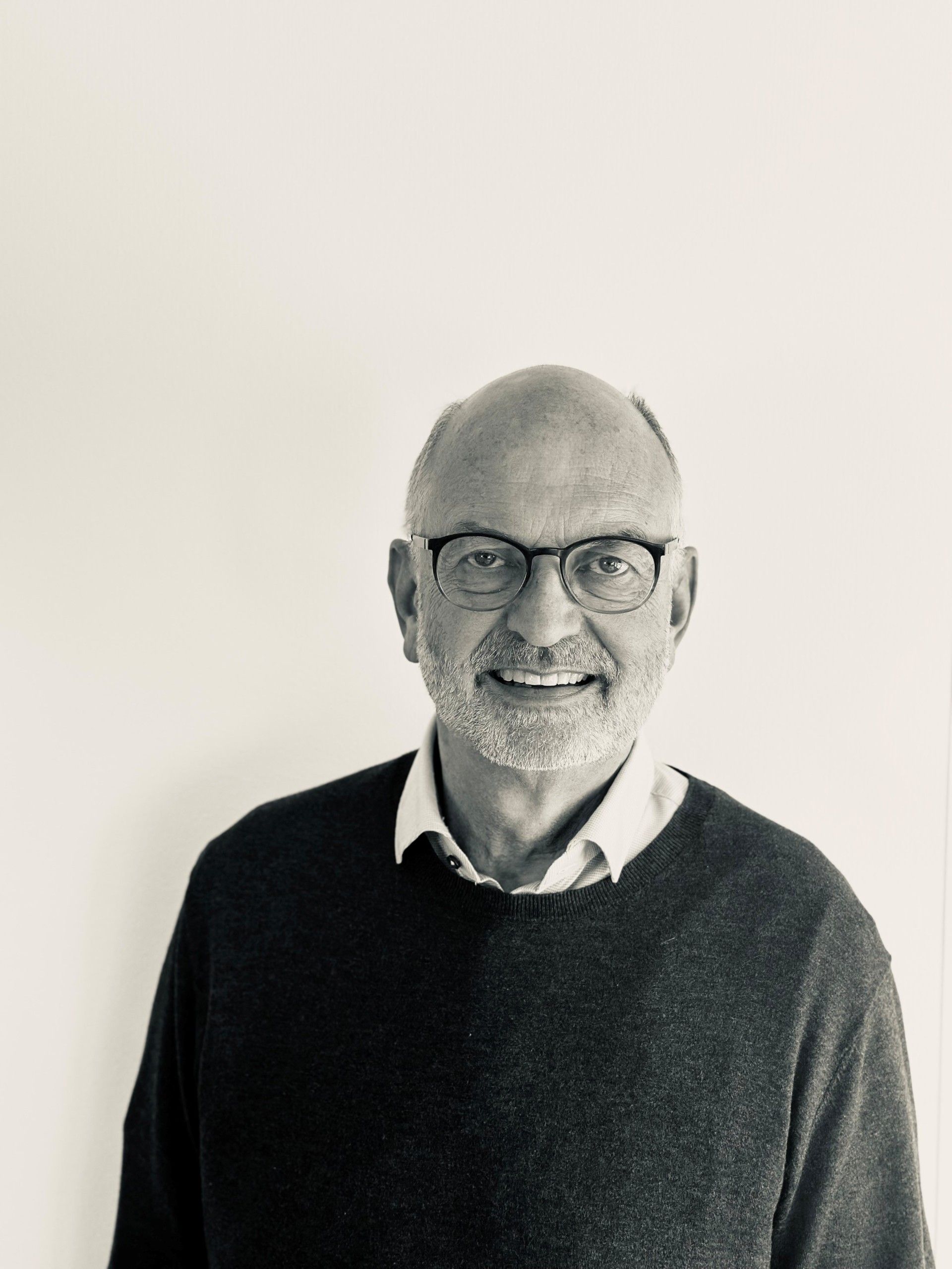 Smiling man in glasses and dark sweater against a plain light background