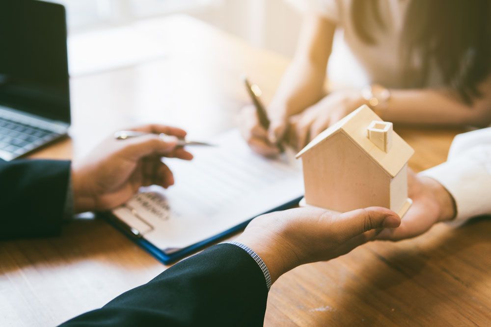 a person is holding a model house while another person signs a document