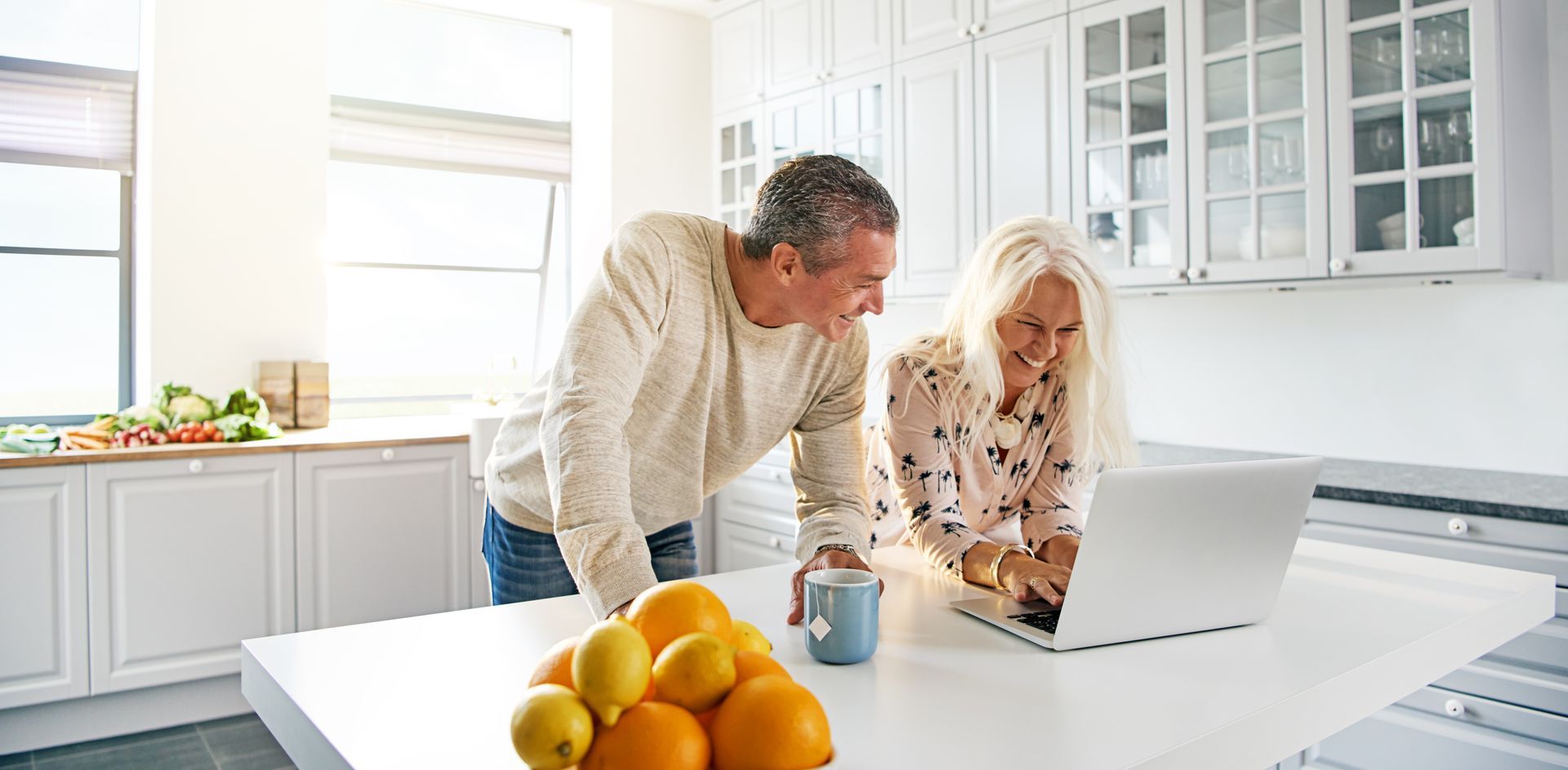 A man and a woman are looking at a laptop in a kitchen.
