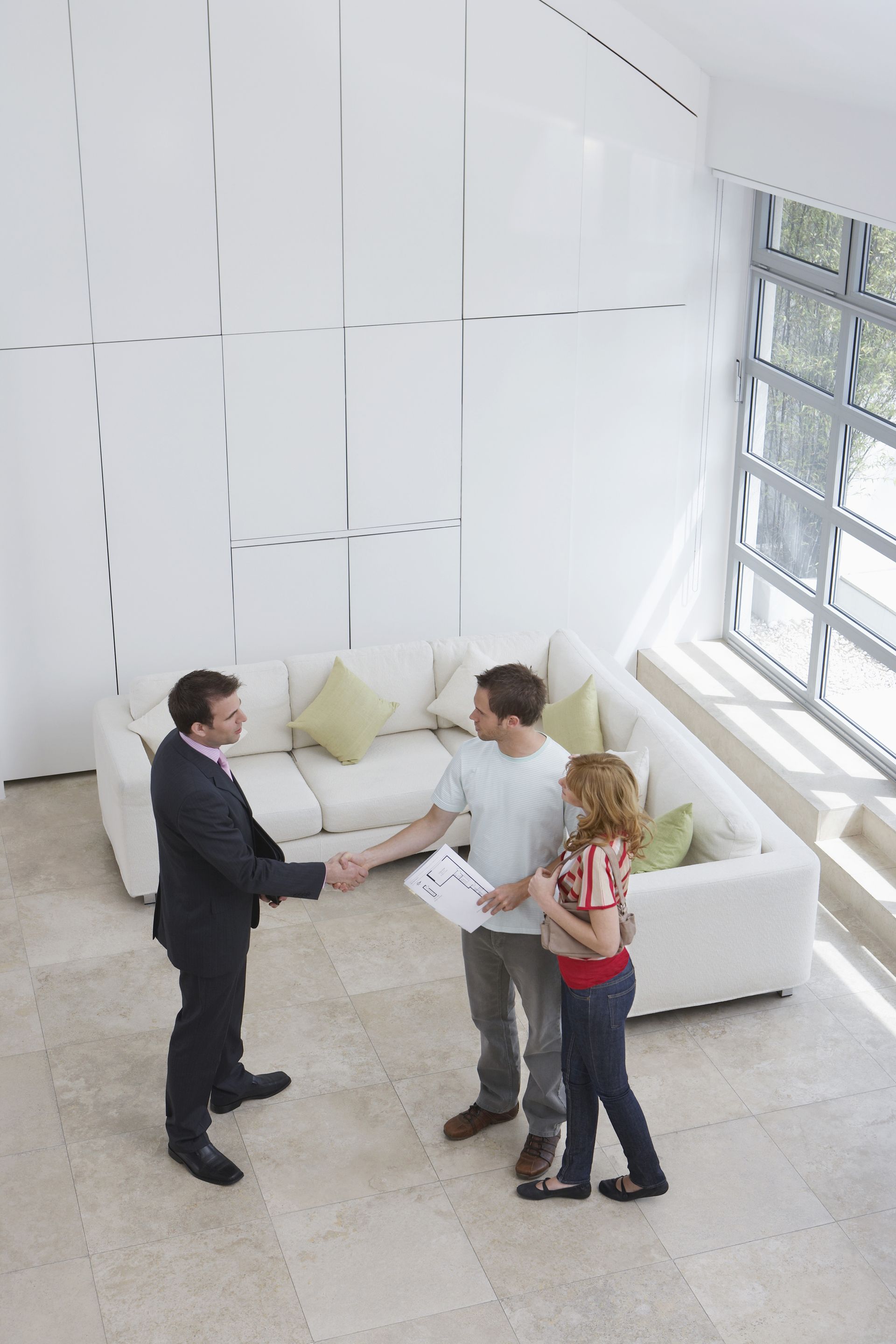 Elevated view of a male real estate agent shaking hands with a man by woman in new home.