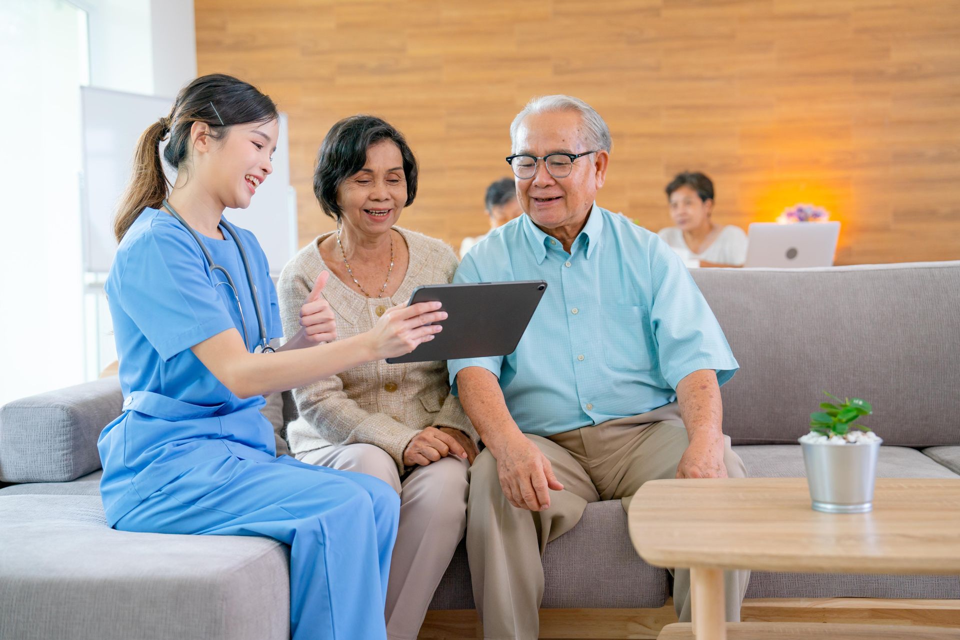 a nurse is showing an elderly couple a tablet while they sit on a couch .