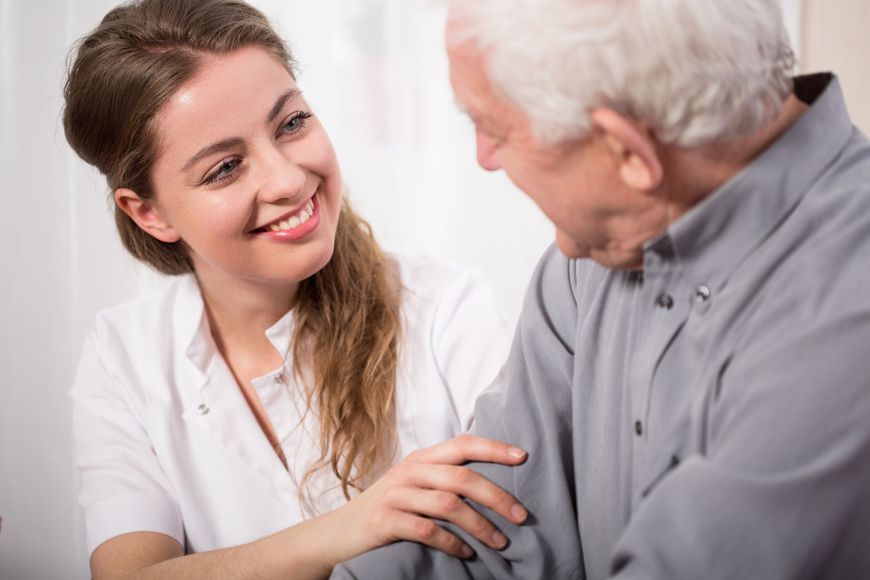 A nurse is talking to an elderly man and smiling.