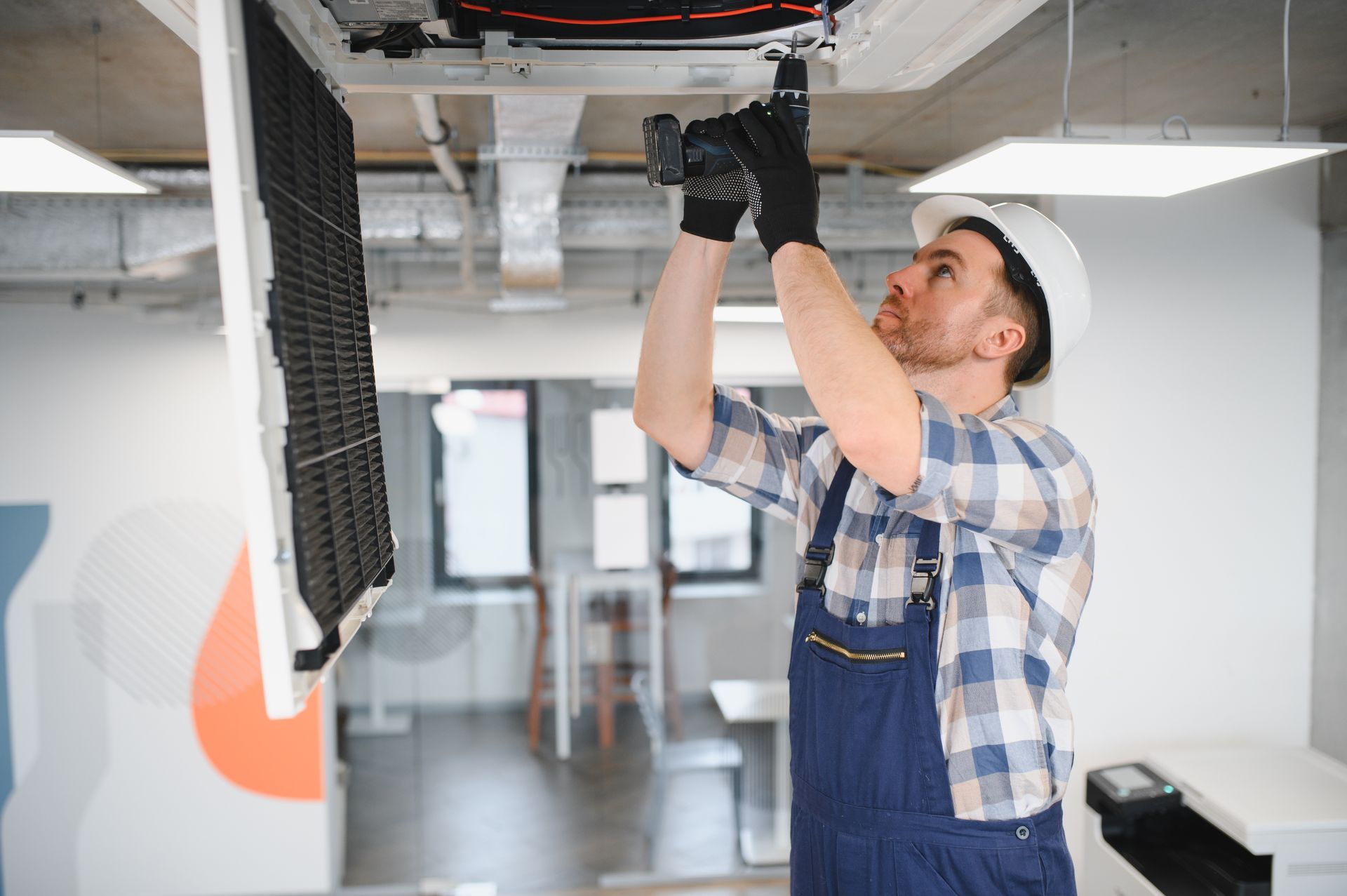 HVAC technician servicing a ceiling-mounted commercial AC unit. HVAC technician servicing a ceiling-mounted commercial AC unit.