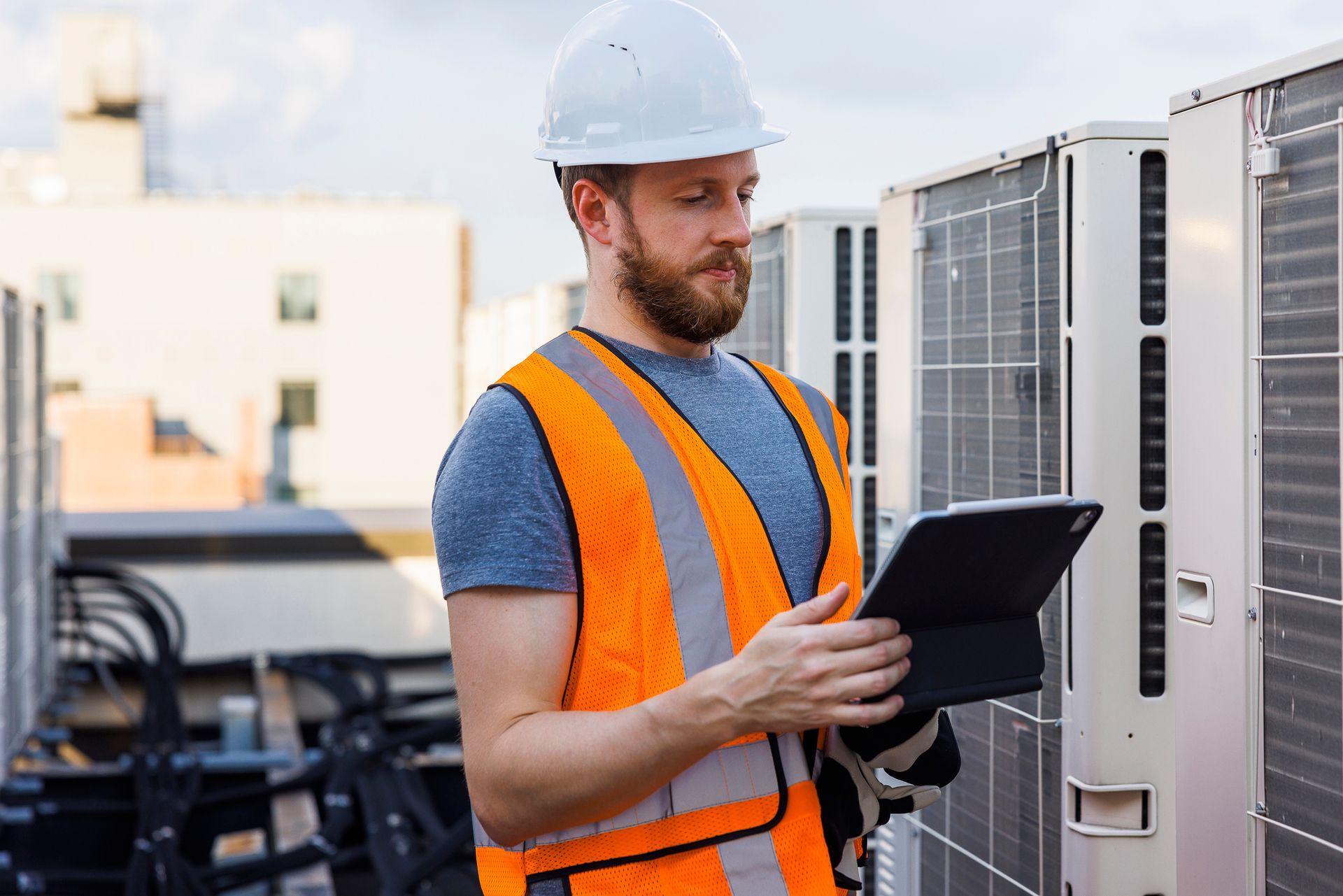 Worker with tablet near rooftop HVAC units.
