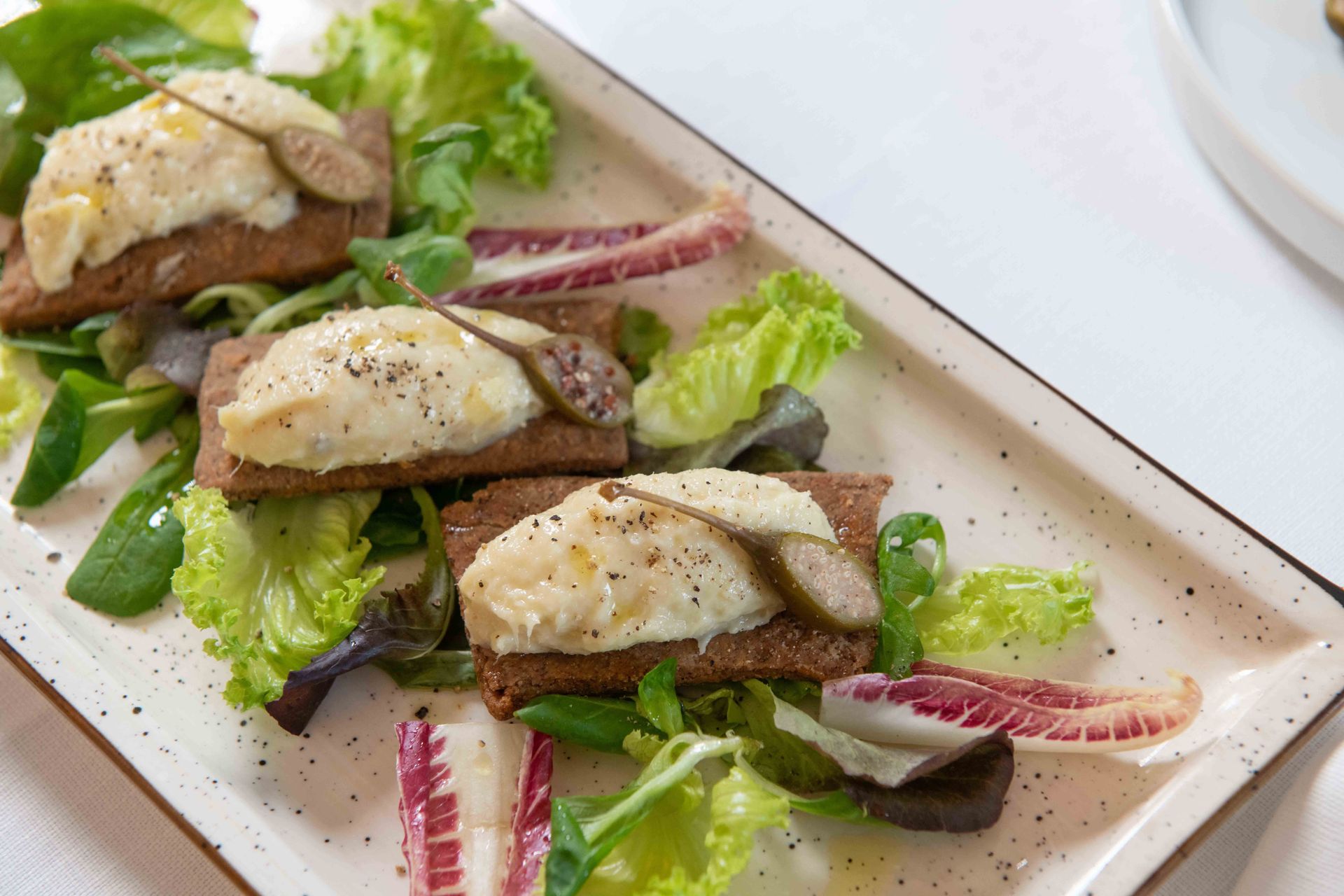 Antipasto: pane di segale con formaggio bianco e capperi, servito con insalata mista su un piatto rettangolare.