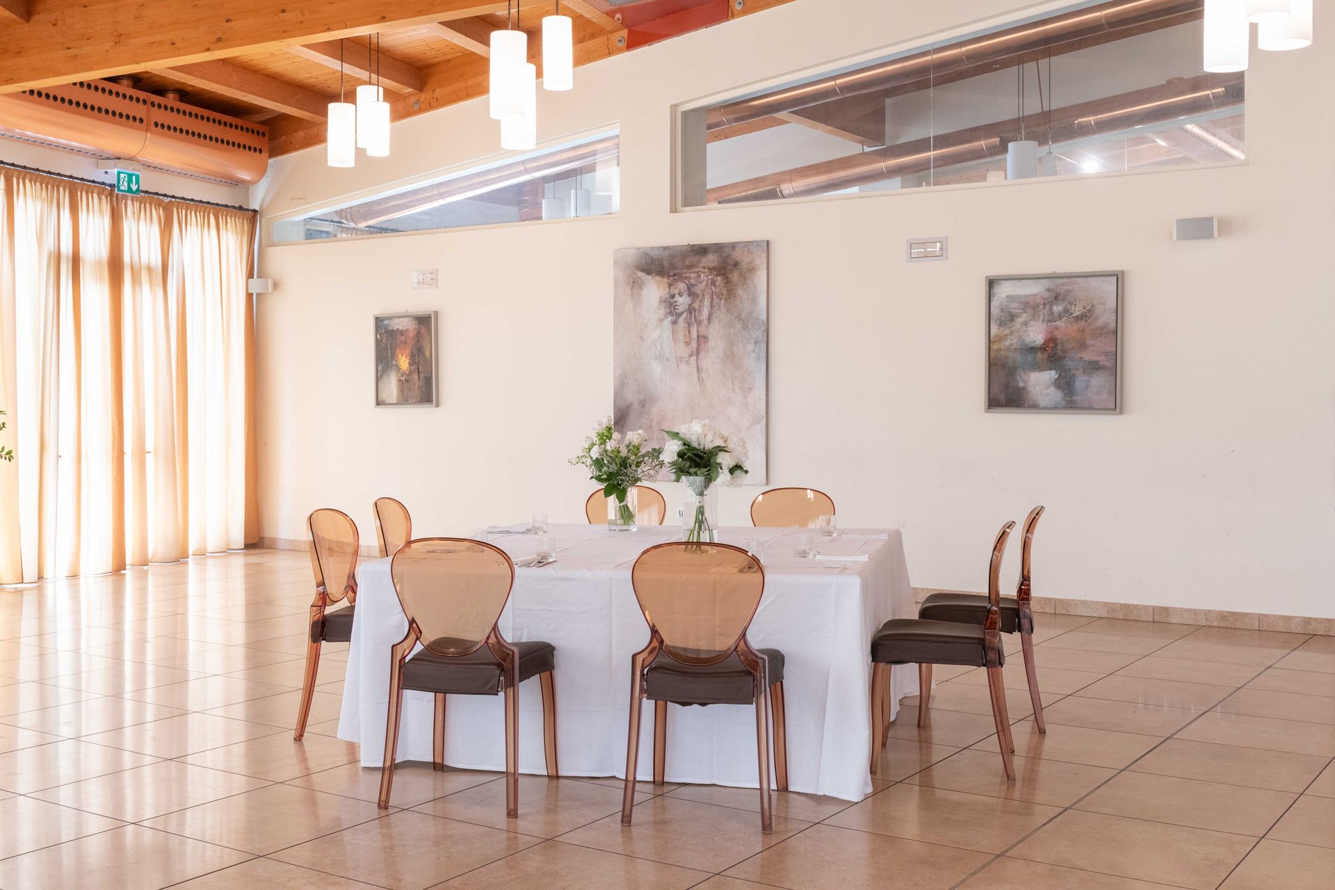 Sala da pranzo con tavolo rotondo apparecchiato per gli ospiti, pareti neutre e soffitto in legno.