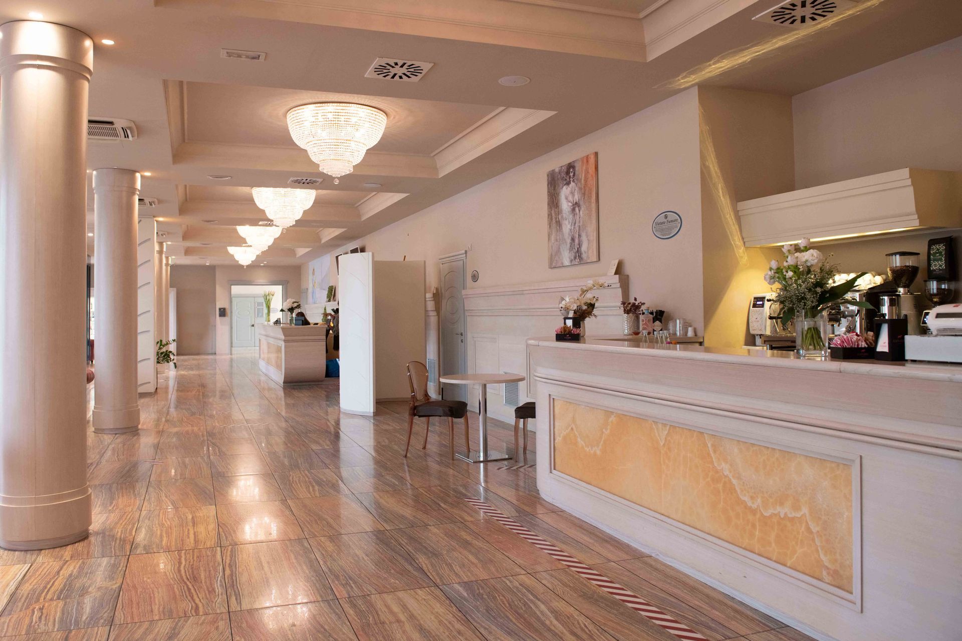 Hall con pavimento in marmo, colonne, lampadari e un bancone della reception bianco.