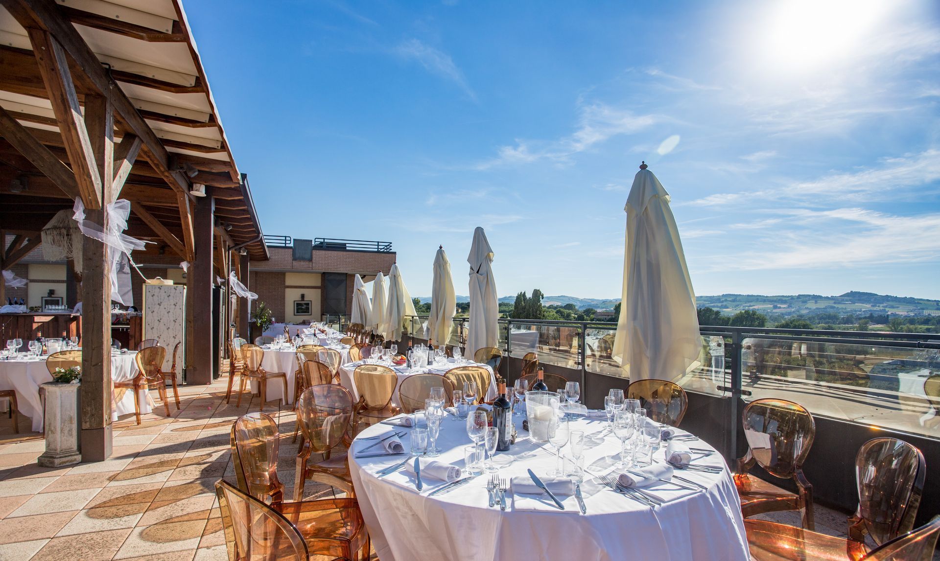 Zona pranzo sul tetto con tavoli apparecchiati per il pasto; cielo azzurro e soleggiato.