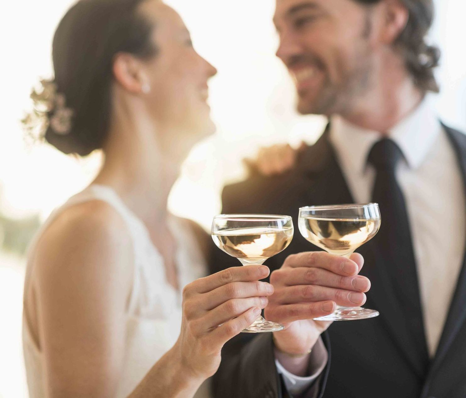 Coppia che brinda allo champagne, sorridente. La donna in abito da sposa, l'uomo in completo.