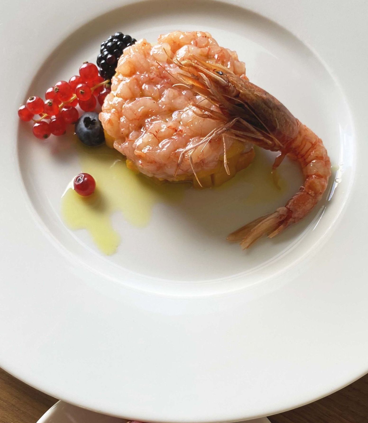 Tartare di gamberi con frutta e olio d'oliva su un piatto bianco.