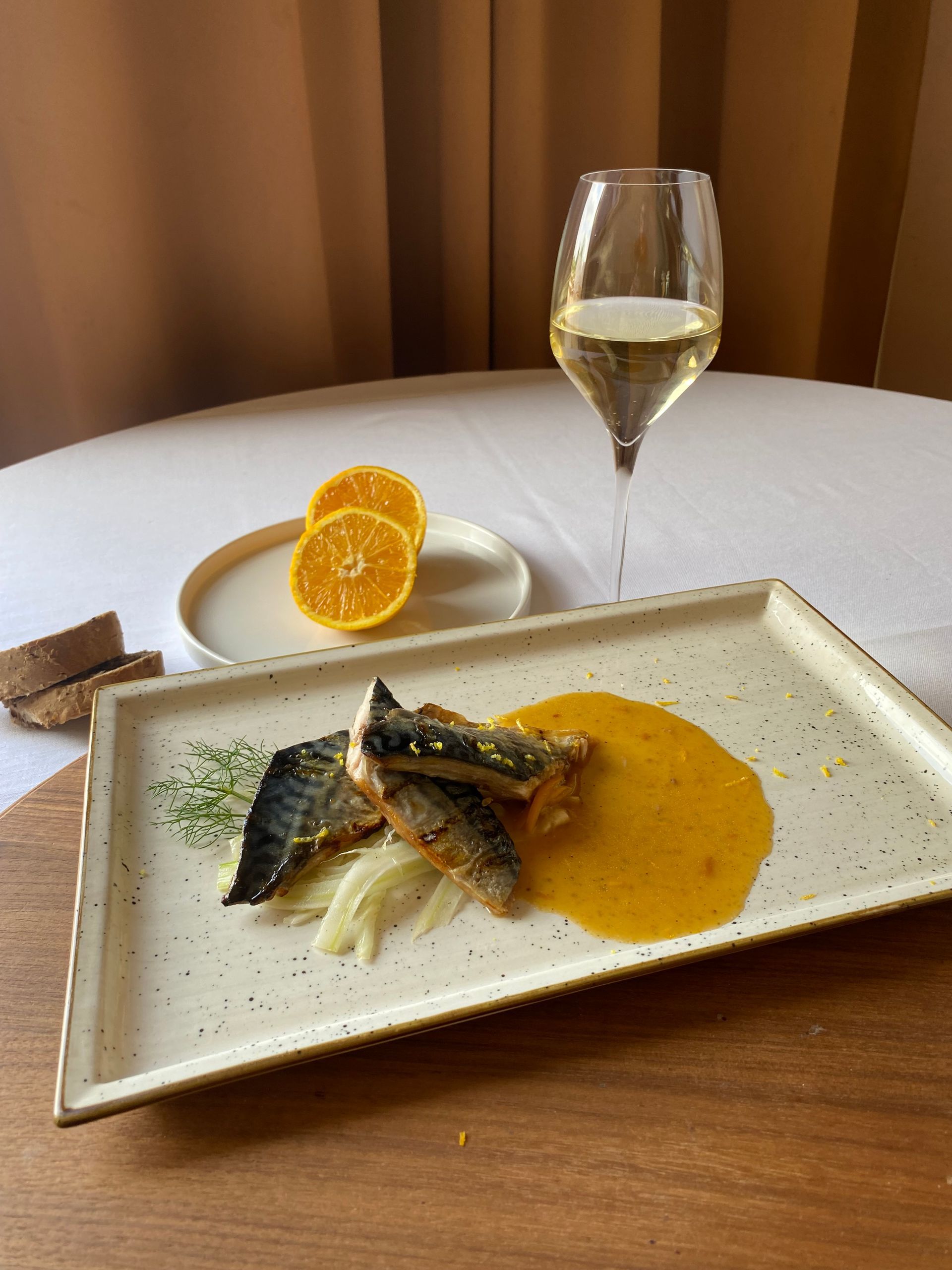 Piatto di sgombro alla griglia con salsa all'arancia, finocchio e vino bianco su un tavolo.