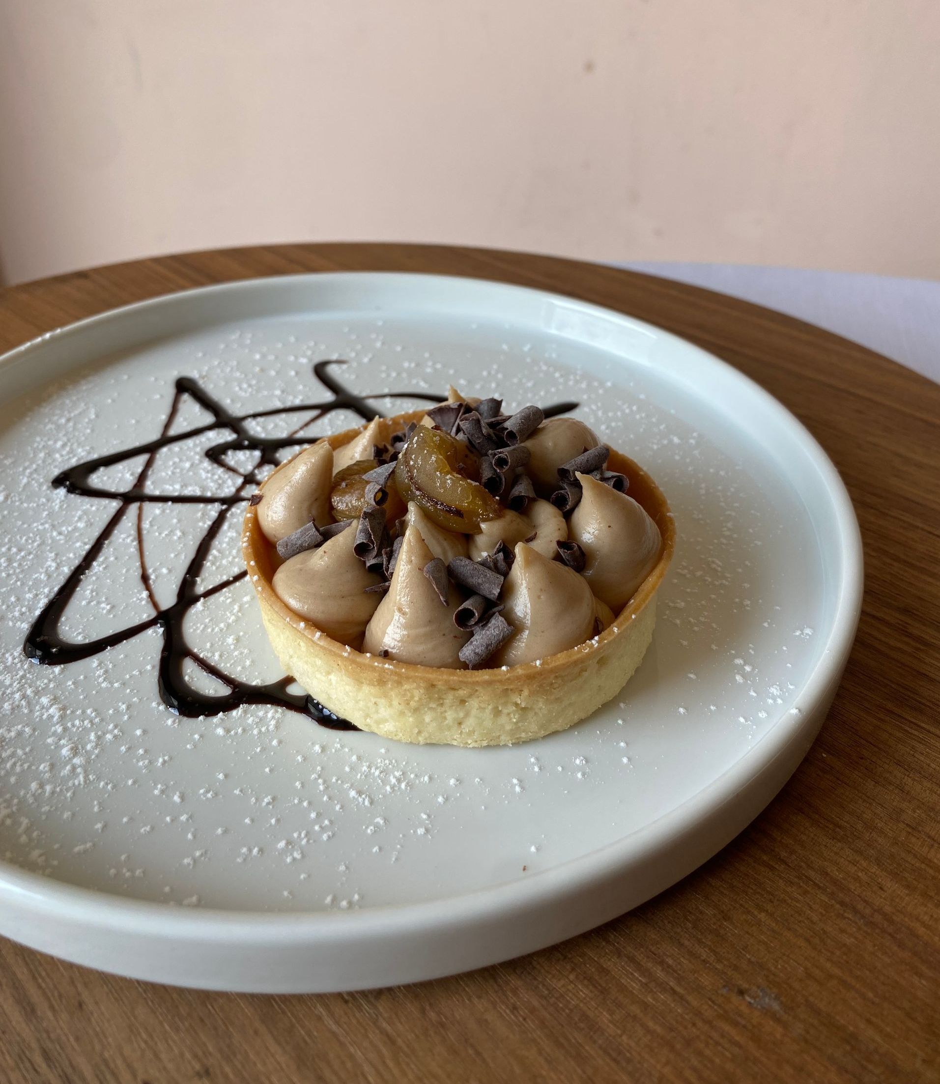 Crostata con ripieno marrone, guarnita con cioccolato fondente e frutta, servita su un piatto bianco con glassa di cioccolato.