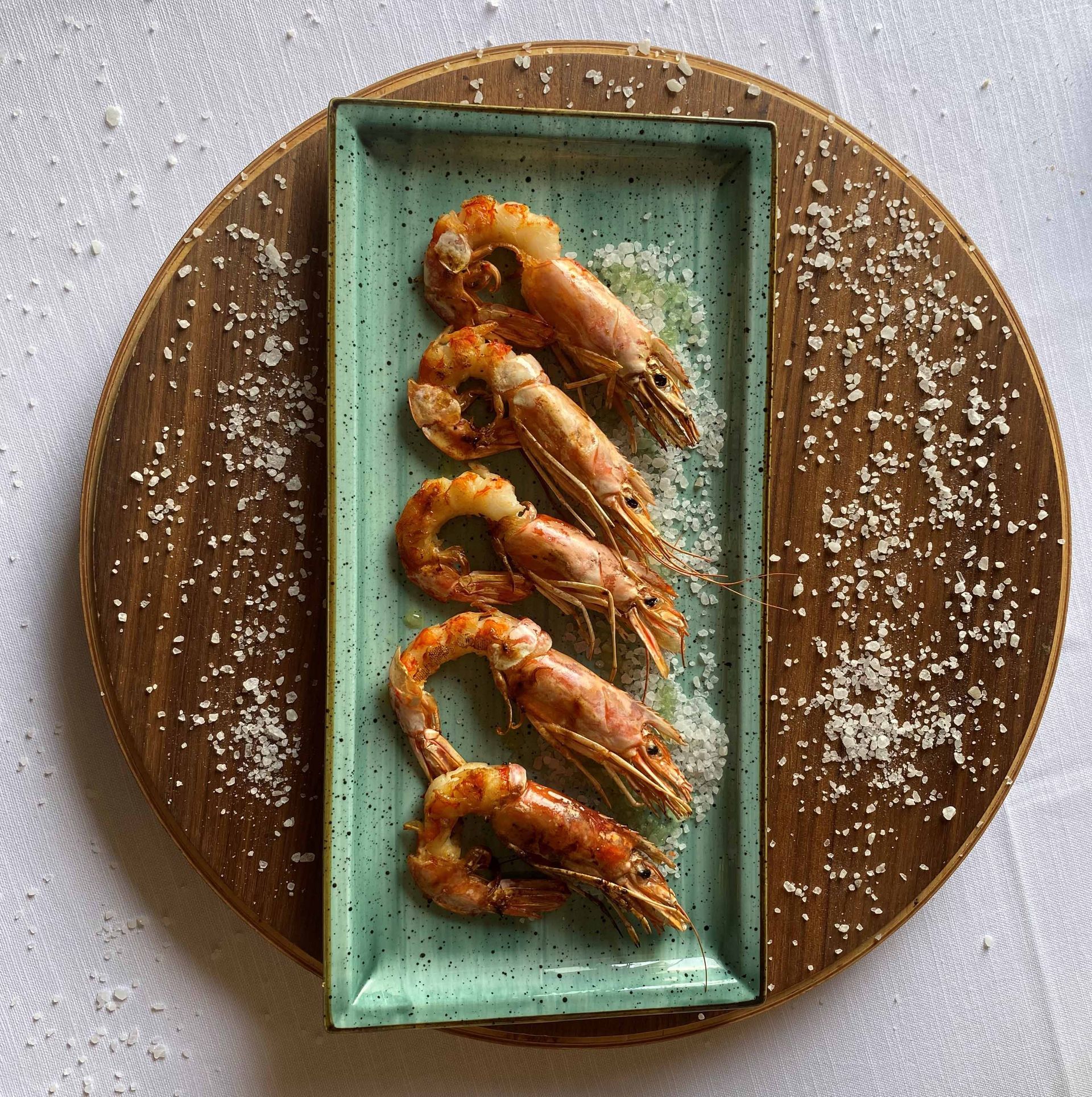 Gamberi grigliati su un piatto rettangolare turchese, disposti su una tavola di legno cosparsa di sale.
