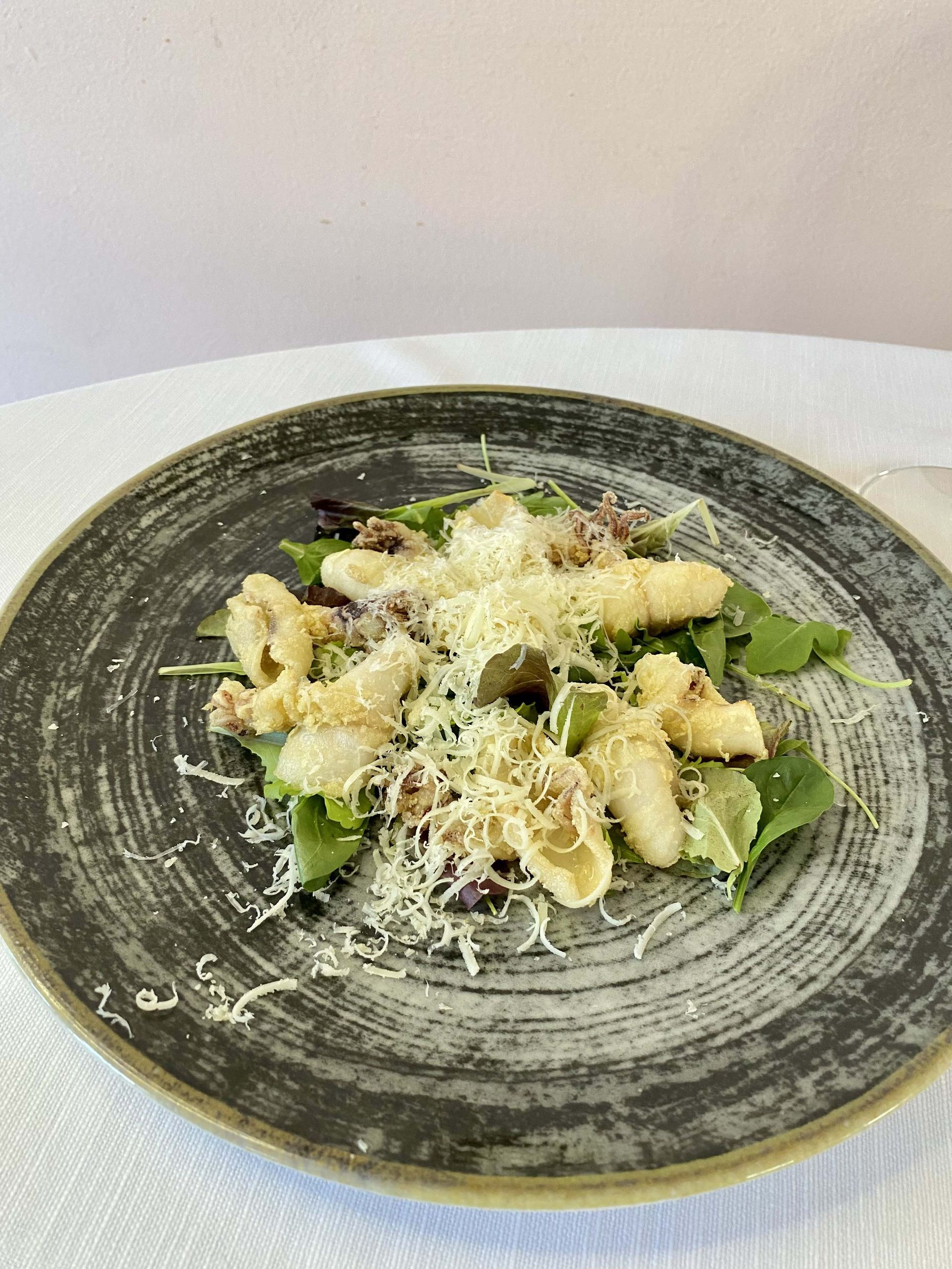 Piatto di cibo fritto, rucola e formaggio grattugiato su un piatto grigio.