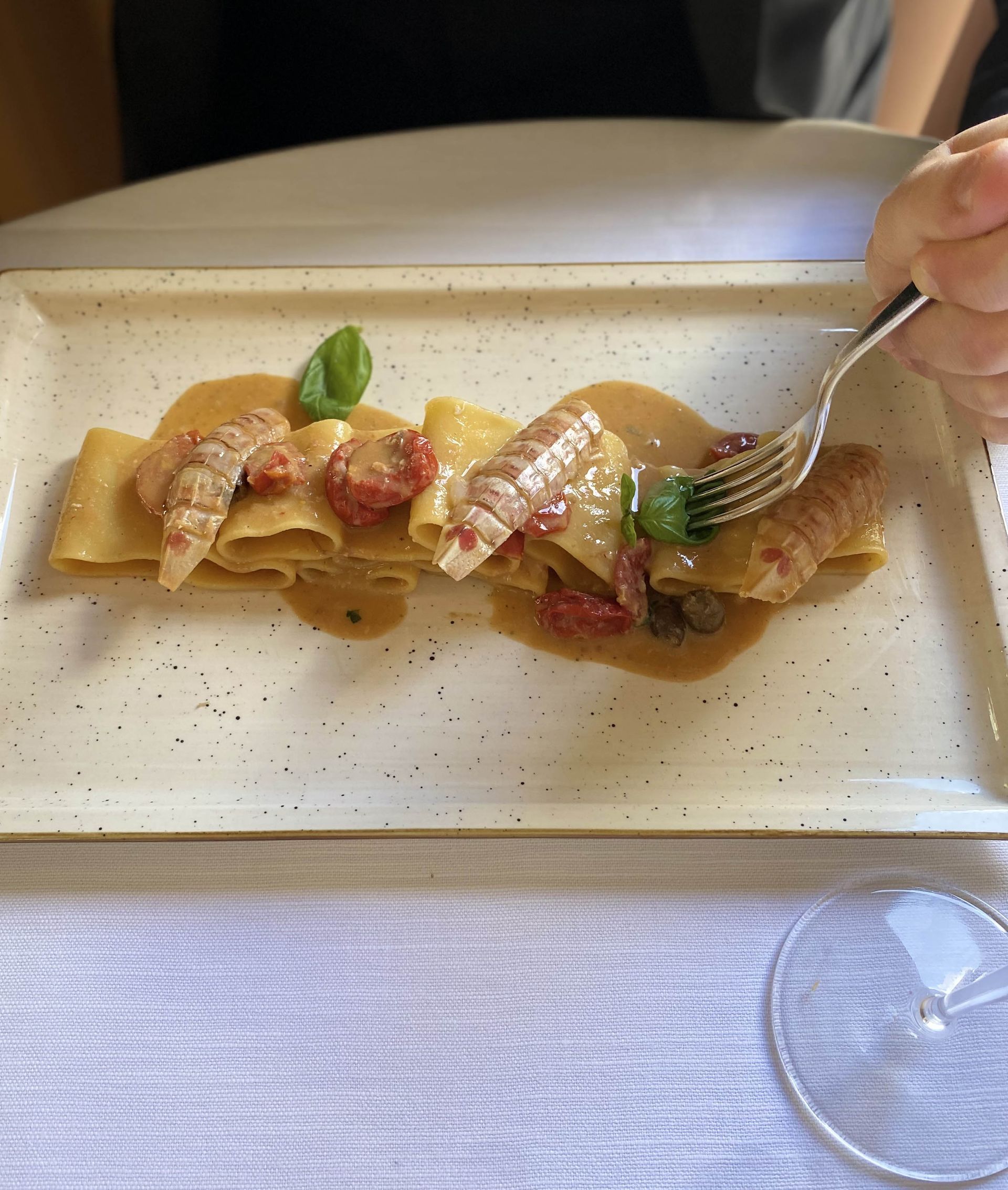 Piatto di pasta con frutti di mare, pomodori e basilico su un piatto rettangolare, con una forchetta in mano.