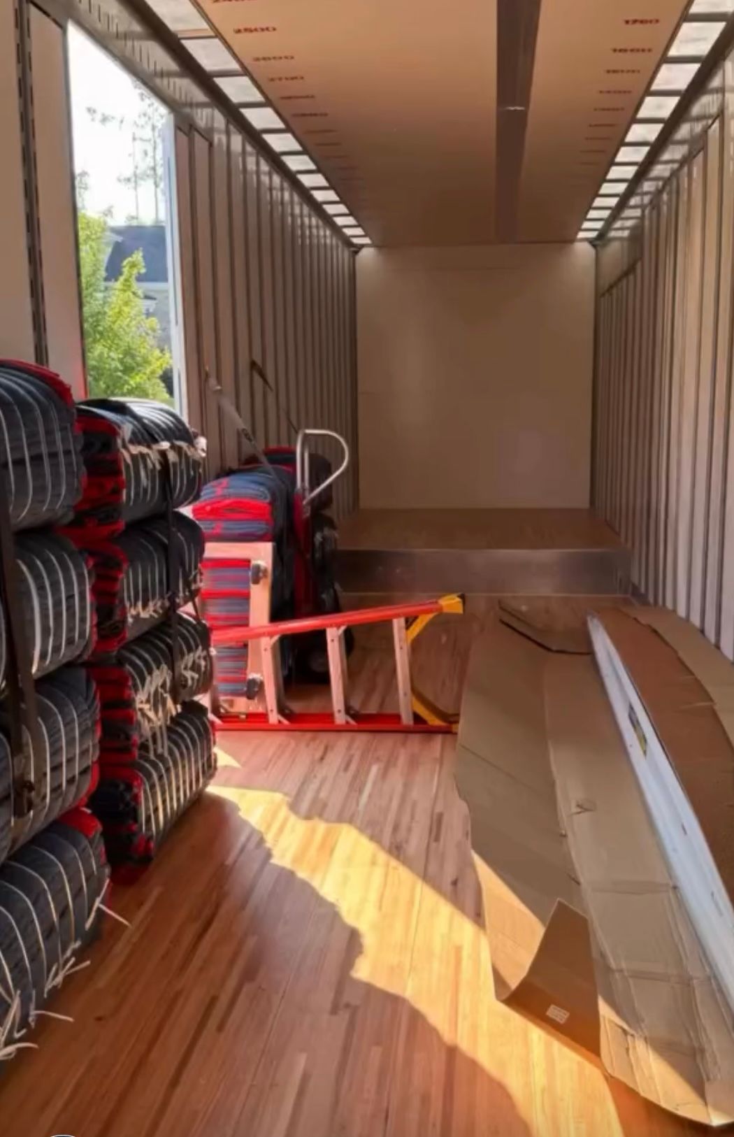 Inside a shipping container; stacks of tires on the left, ladder in the middle, wooden floor, sunlight streaming in.