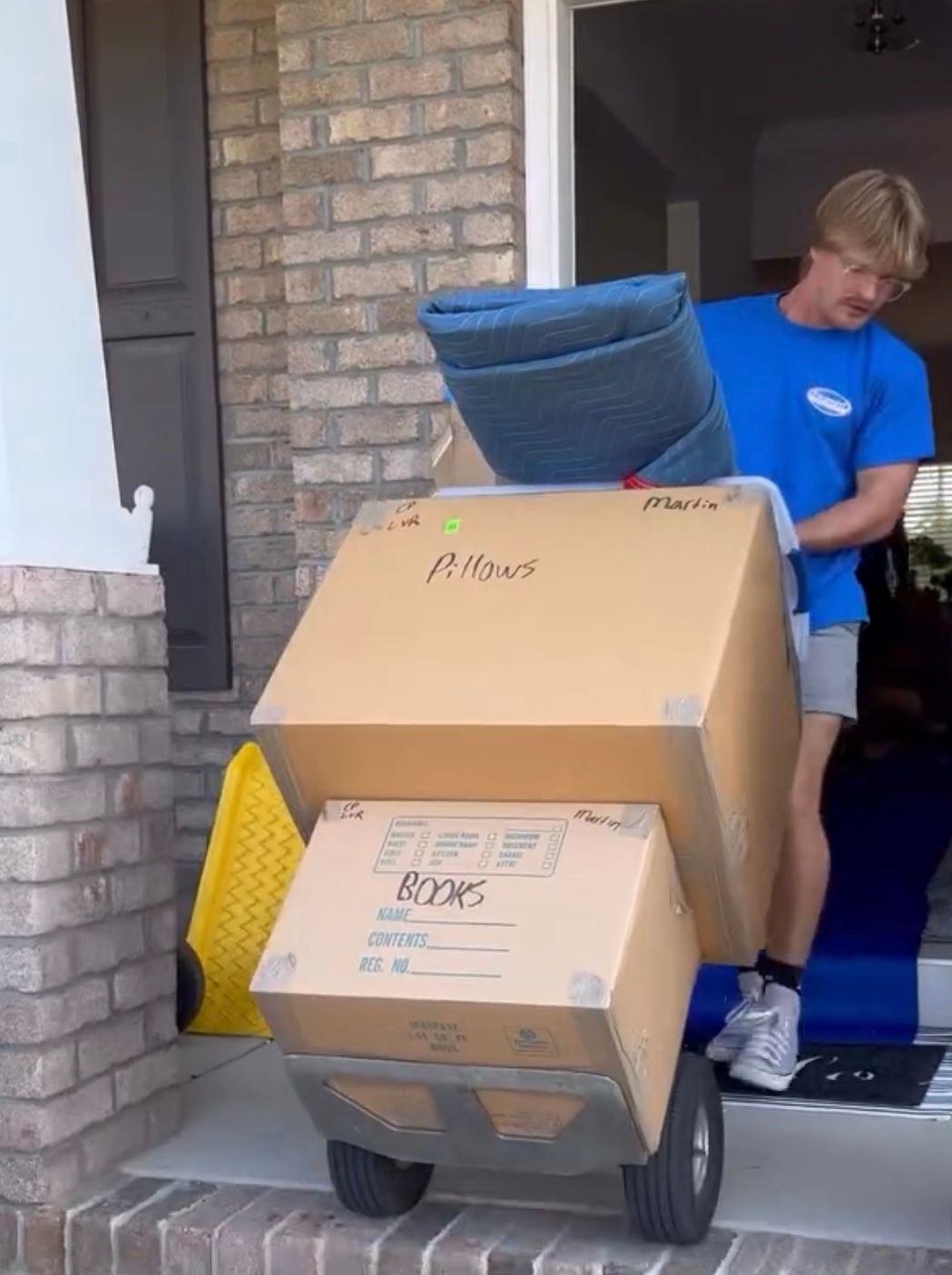 Young man pushing boxes on a dolly out of a doorway. Boxes are labeled
