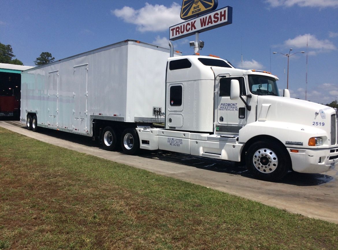 White semi-truck at a truck wash. The truck is parked on a paved surface with grass in the foreground under a blue sky.