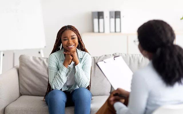 A woman is sitting on a couch talking to a therapist.